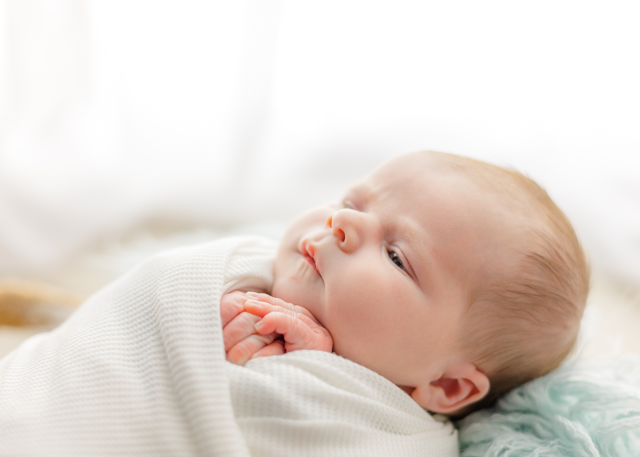 A newborn baby lays in a white swaddle with eyes open