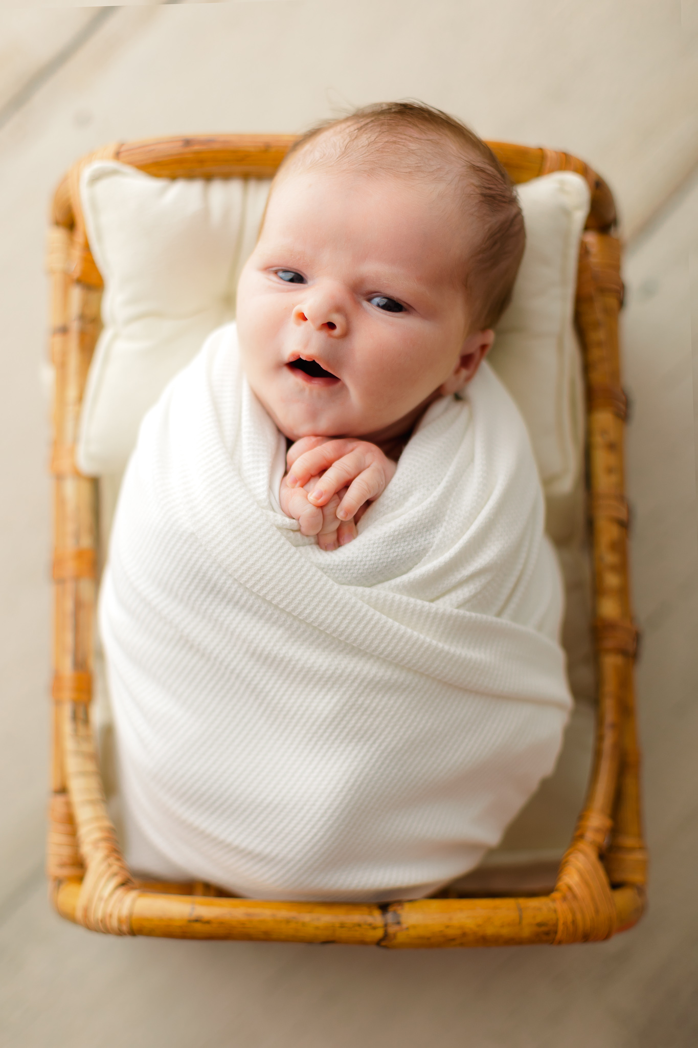 A newborn baby lays in a wicker crib wrapped in a white swaddle with eyes open precious glimpse ultrasound