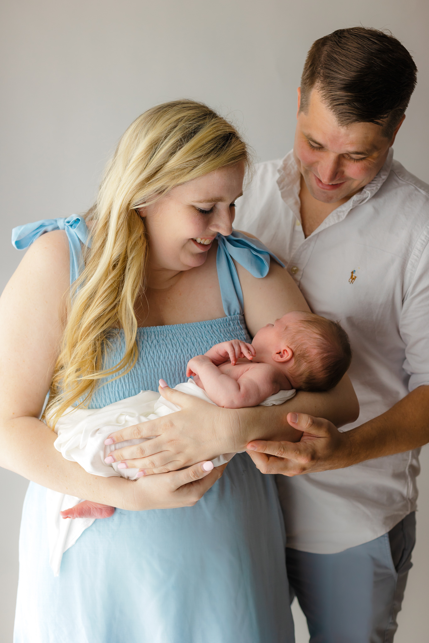 A mother cradles her newborn baby in a blue dress while dad leans in over her shoulder savannah birth center