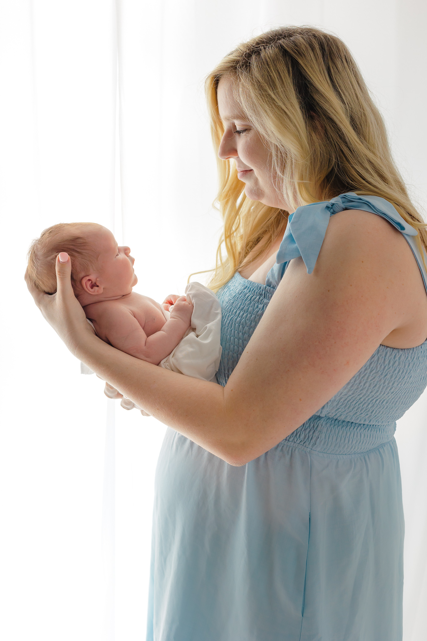 A new mom stands in front of a window looking down at the newborn baby in her arms savannah birth center