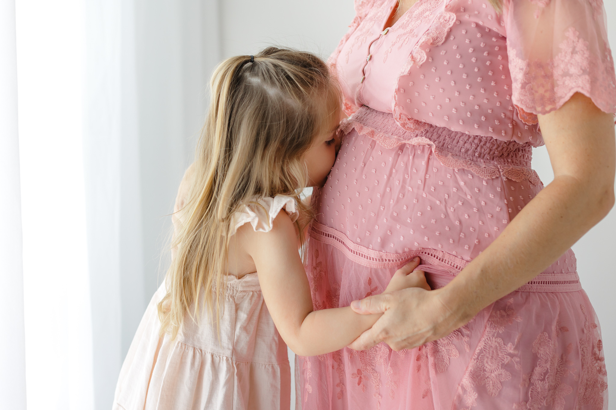 A young girl kisses the bump of her pregnant mother in a pink dress prenatal massage Savannah