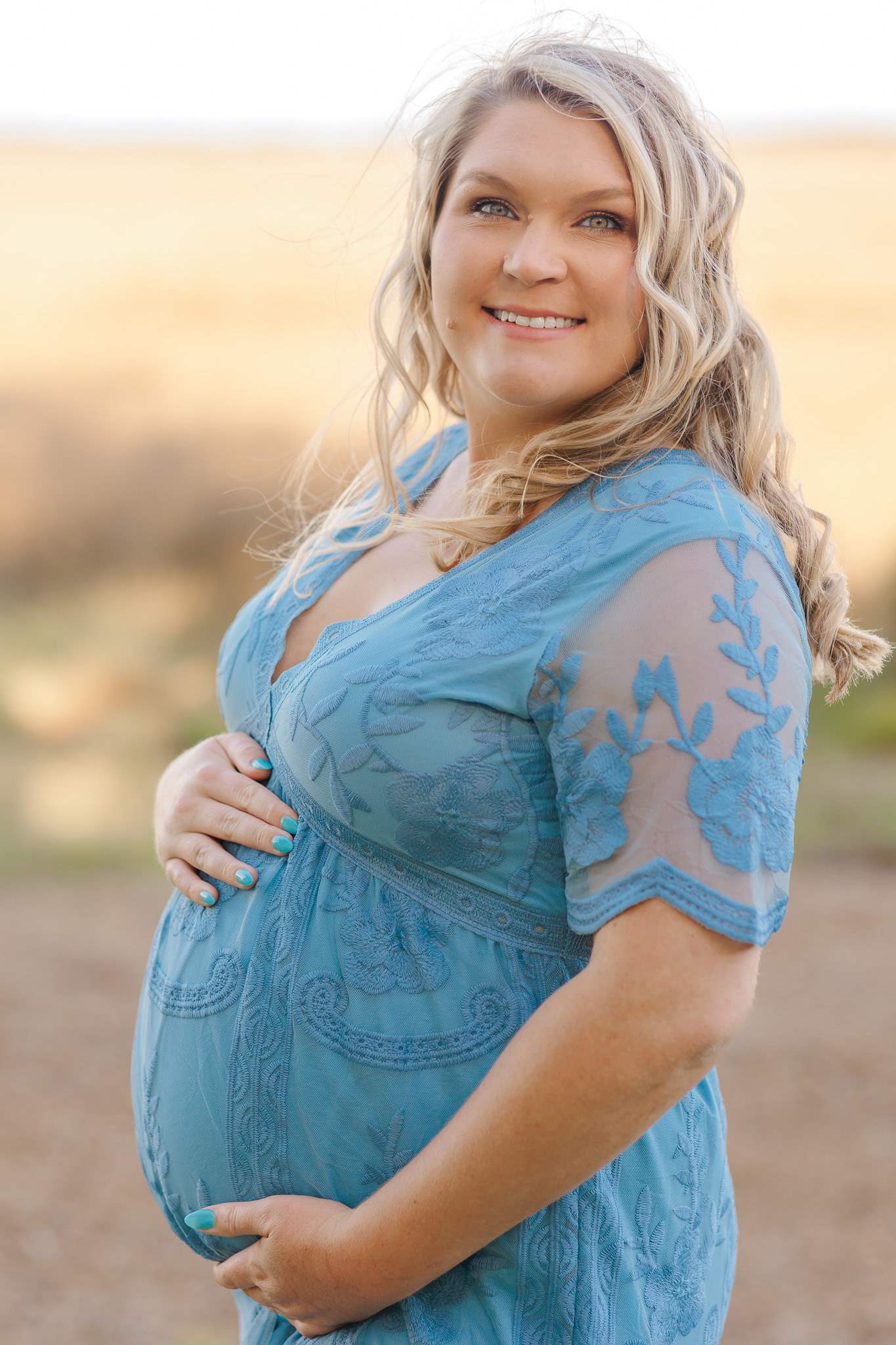 A mother to be stands in a park wearing a blue lace maternity gown prenatal yoga Savannah