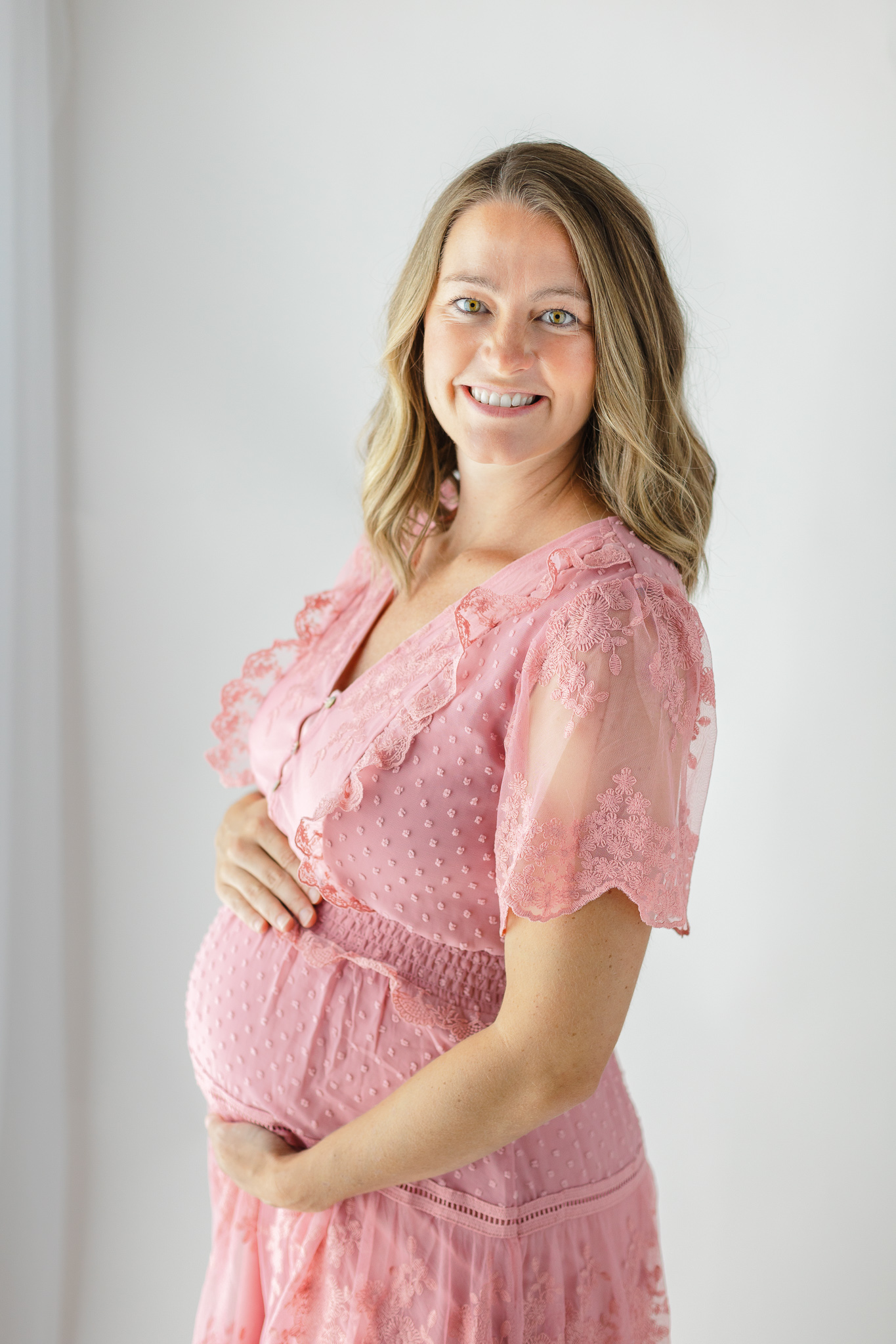 A mother to be holds her bump in a pink dress in a studio