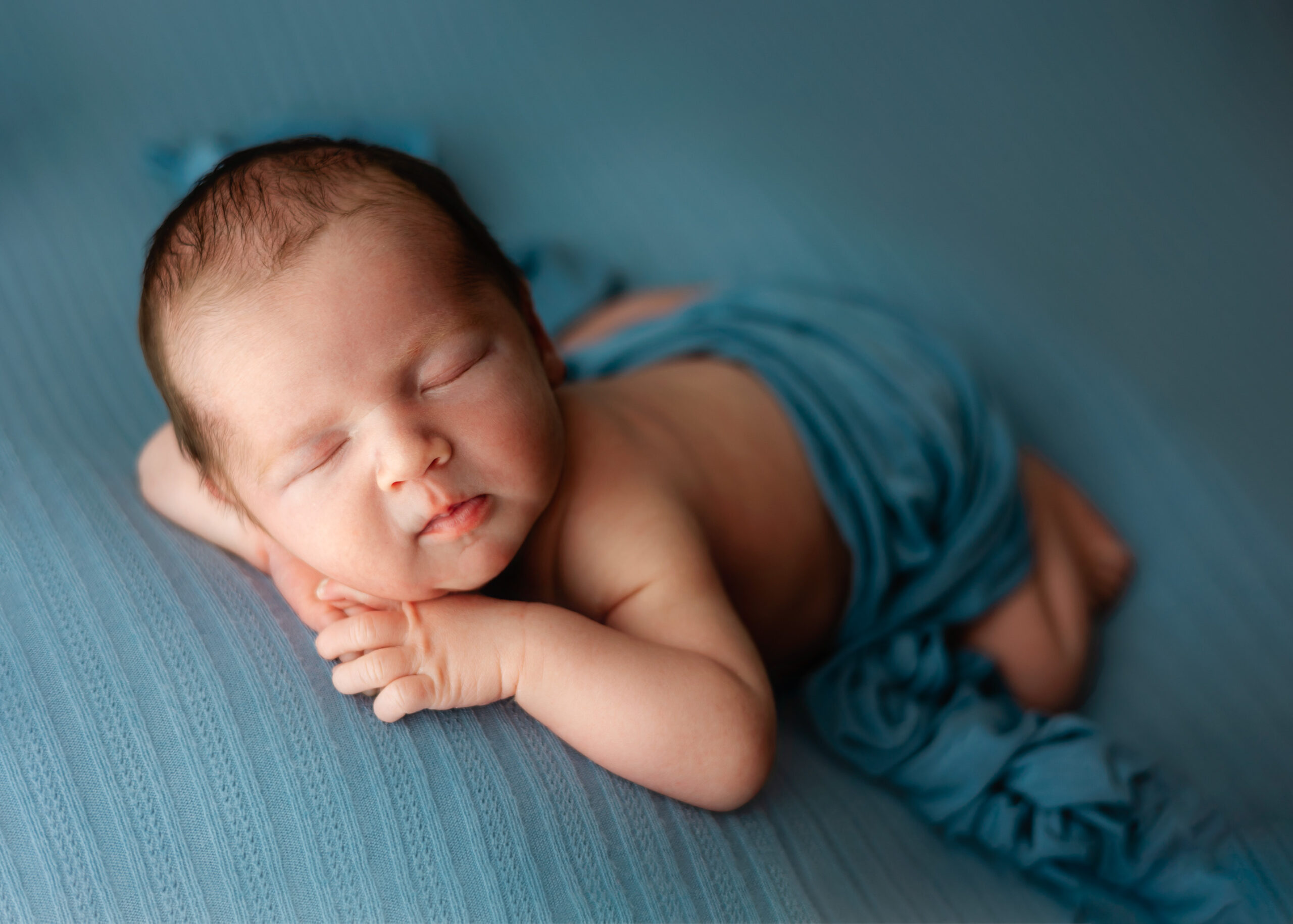 A sleepy boy newborn baby posing with chin on hands on blue fabric pediatricians in Pooler