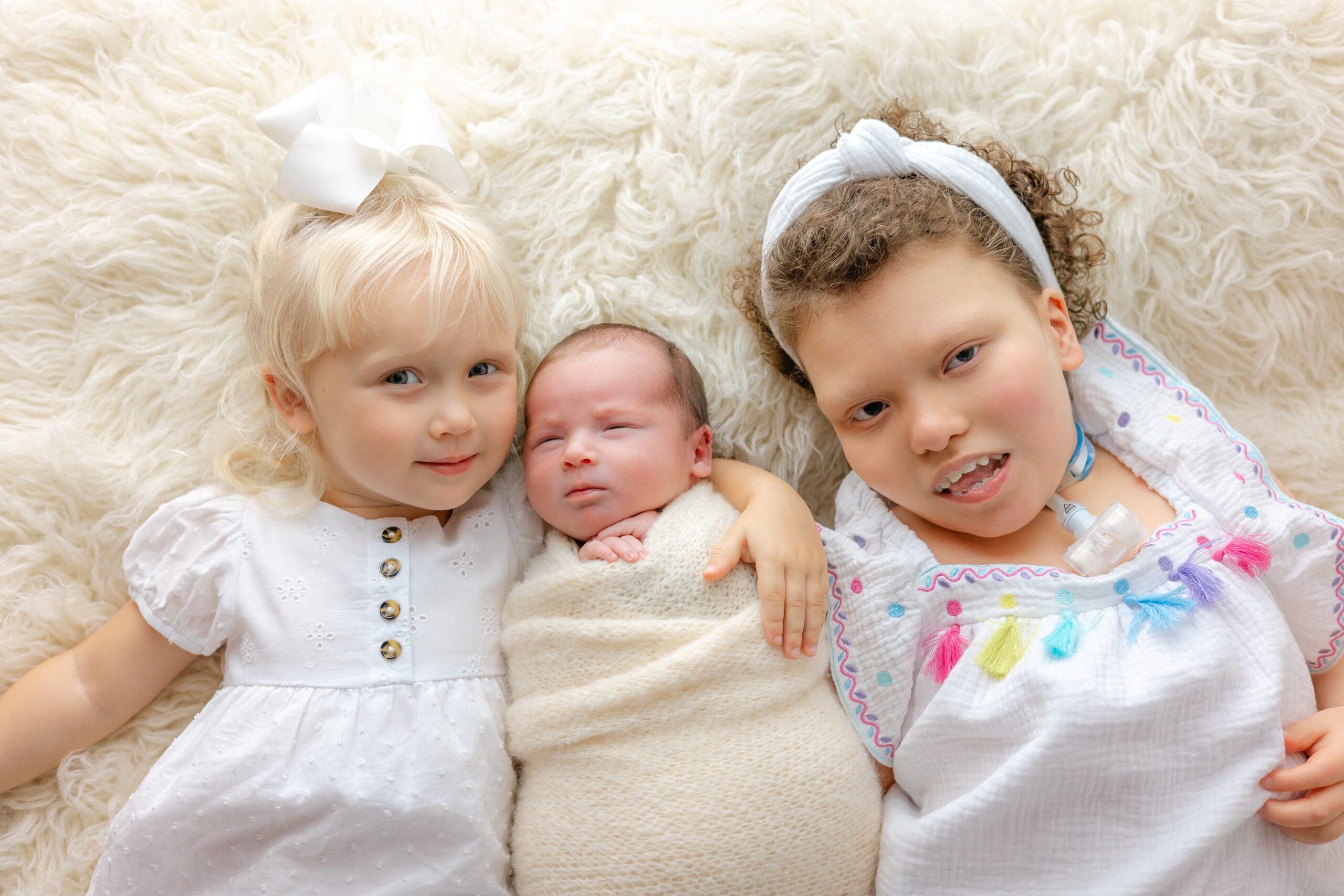 A sleepy newborn baby in a white swaddle lays on a bamboo basket surrounded by his sister pediatricians in Pooler