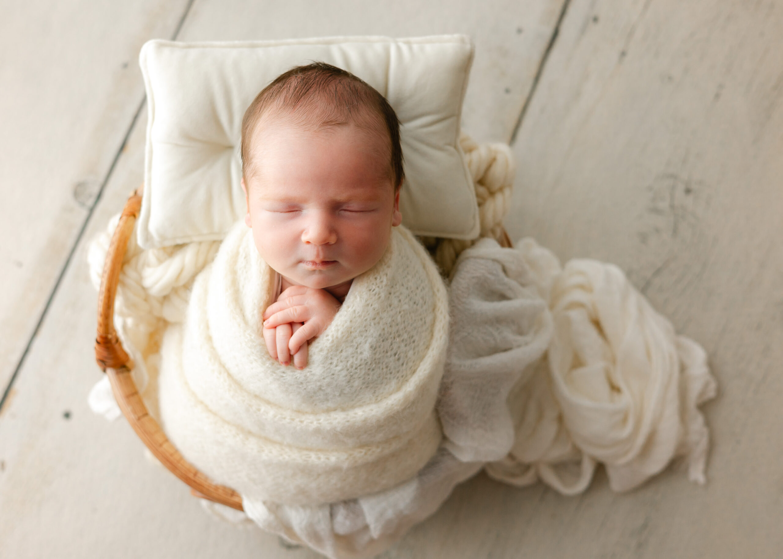 A sleepy newborn baby in a white swaddle lays on a white blanket in a bamboo basket pediatricians in Pooler