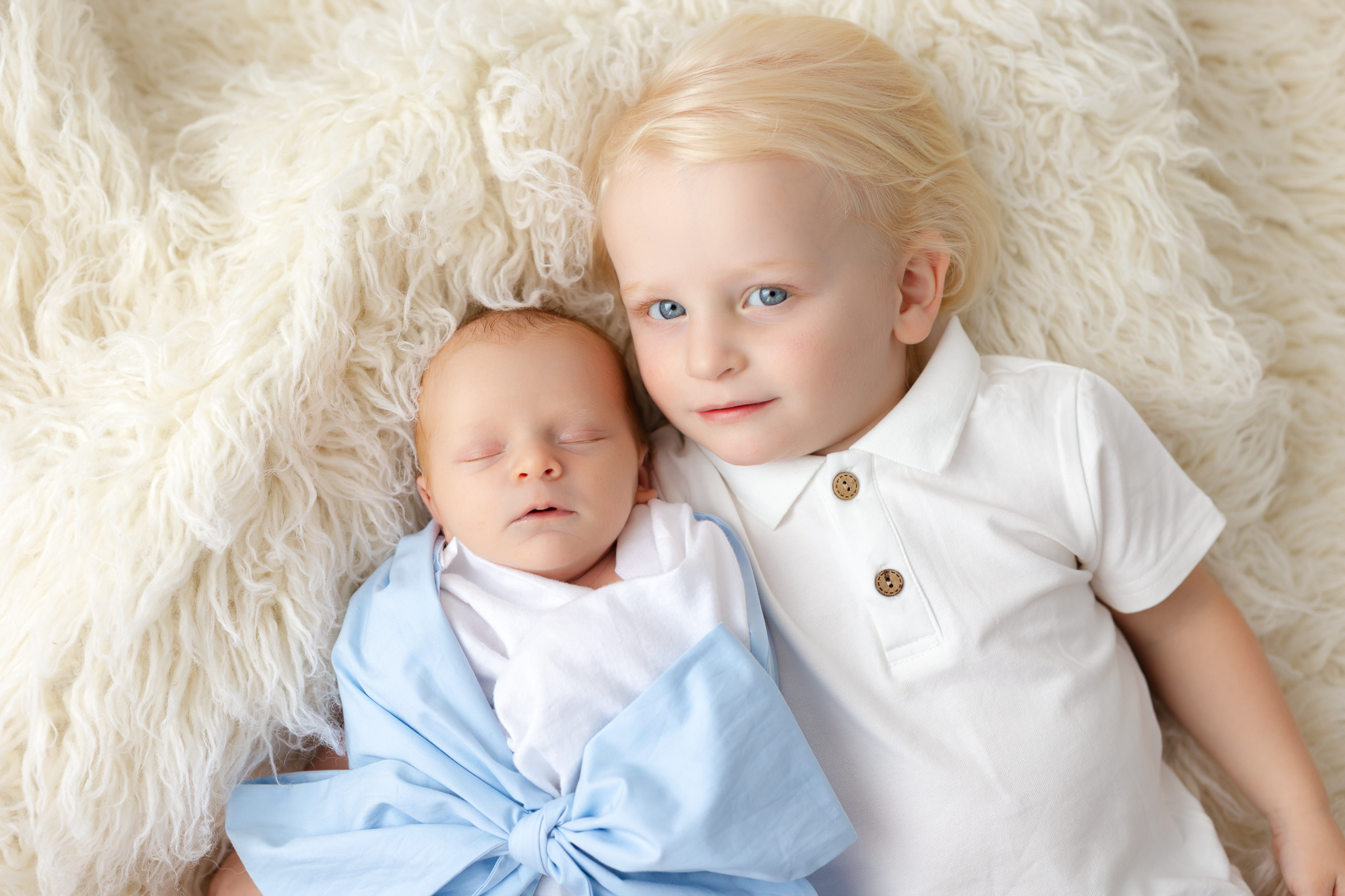 Newborn boy laying down with his older toddler brother. 