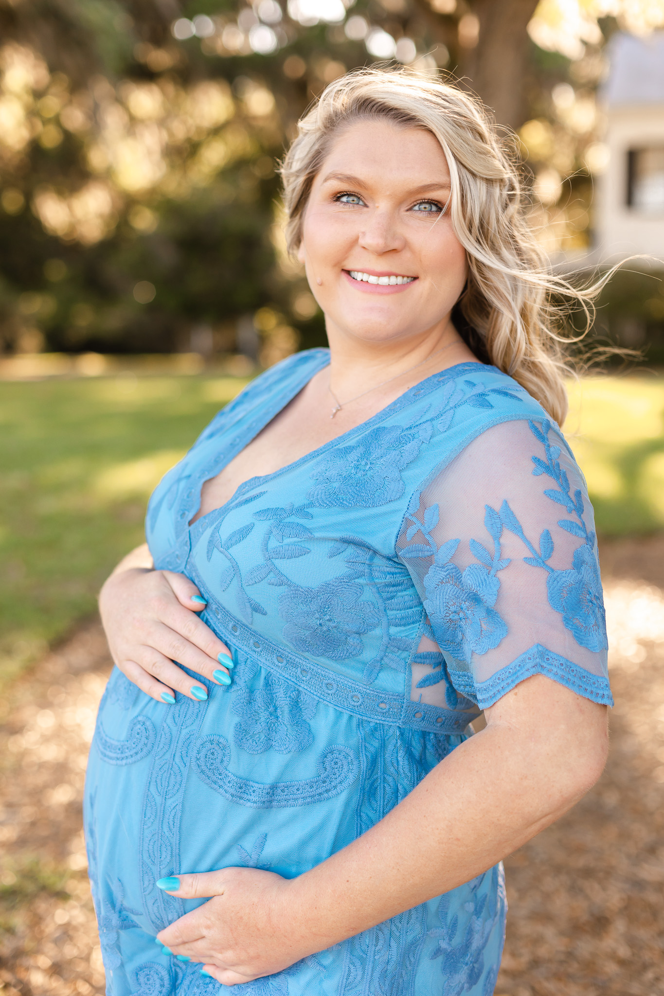 A mother to be stands in a park on a windy day while holding her bump savannah fertility clinic