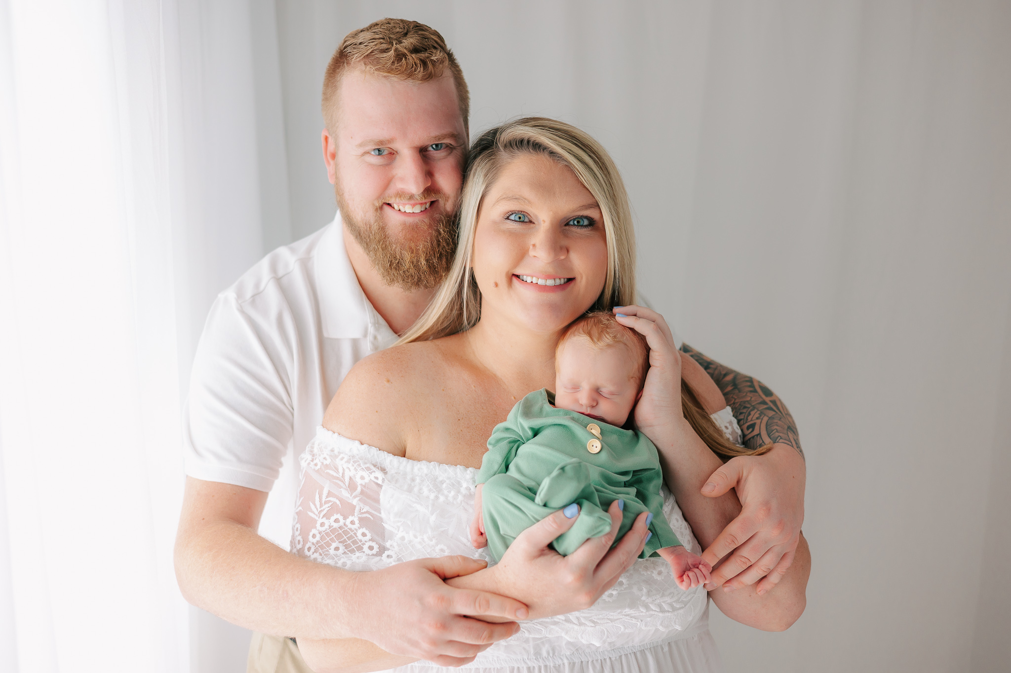 New parents hug while standing in a studio holding their sleeping newborn baby mommy and me classes savannah ga