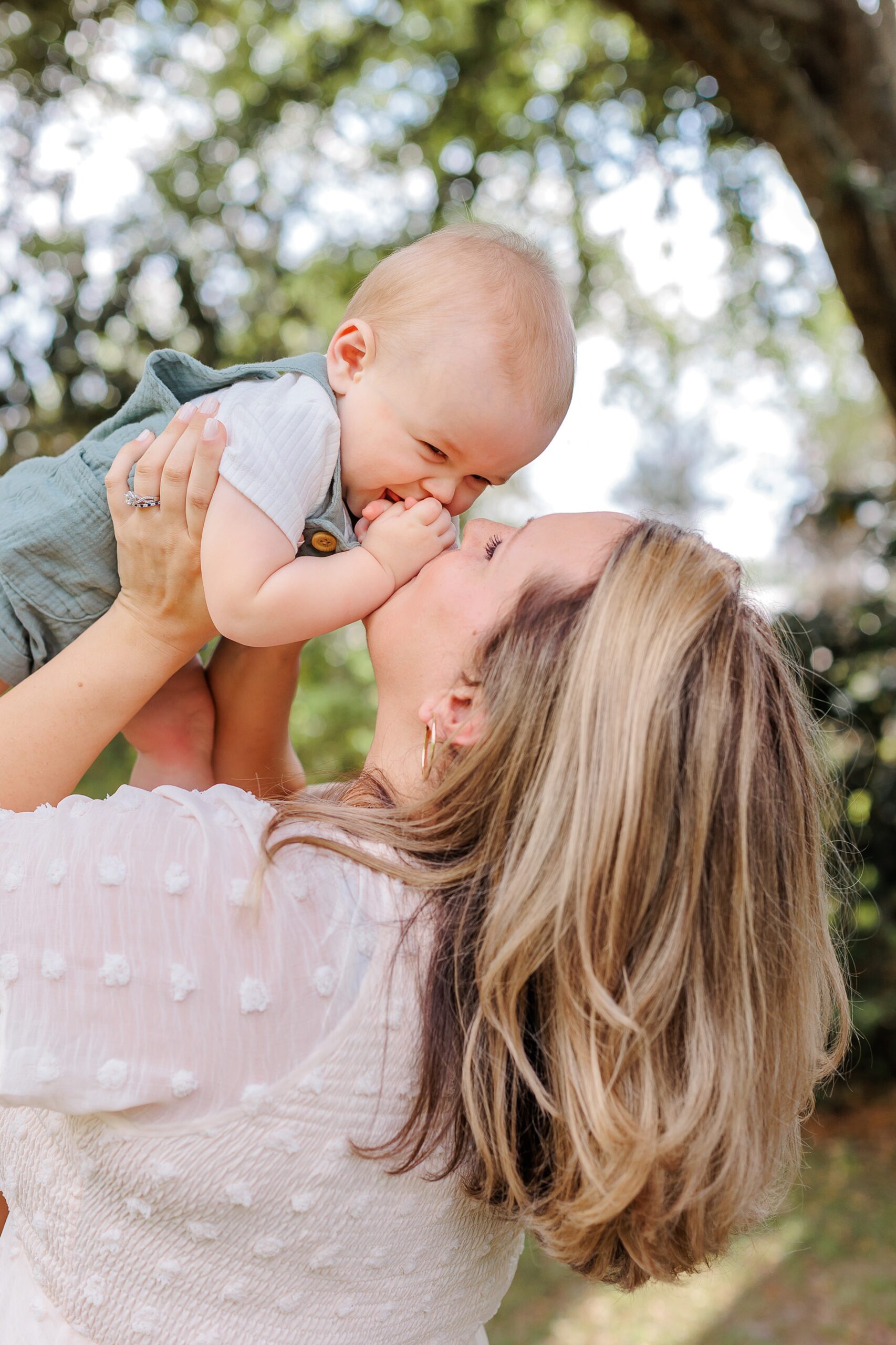 A mom in a white dress plays with her infant son abover her head nannies in Savannah