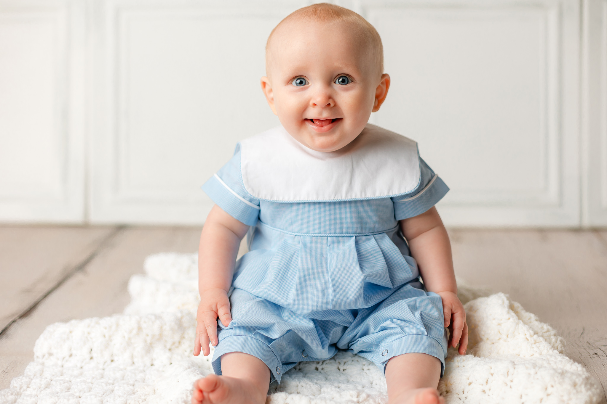 A young boy sits in a blue outfit with white collar on a knit blanket on the floor of a studio peaches savannah ga