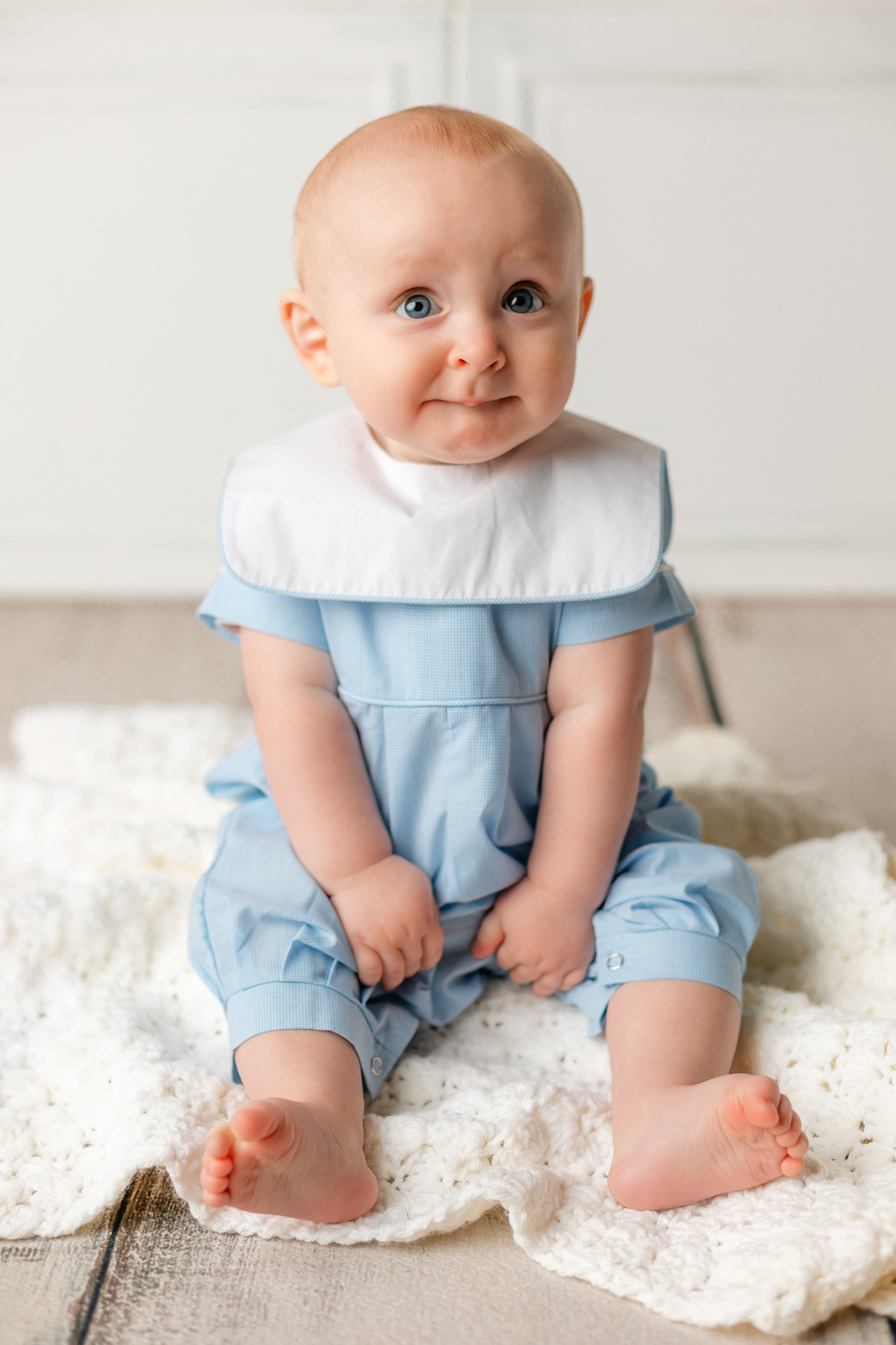 A young baby sits upright on the floor of a studio in a blue outfit