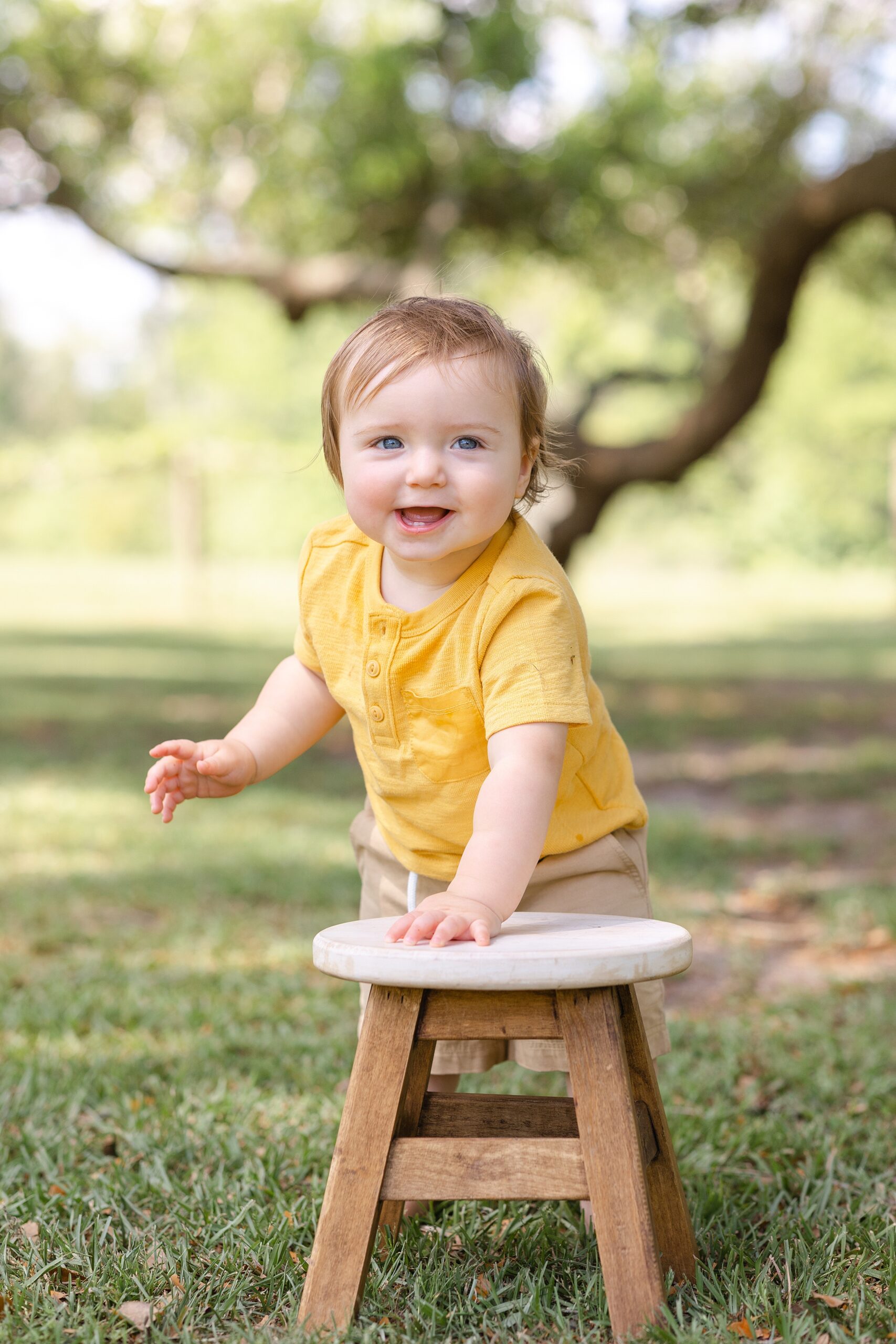 A toddler boy in a yellow shirt stands while holding on to a small wooden stool at savannah playgrounds