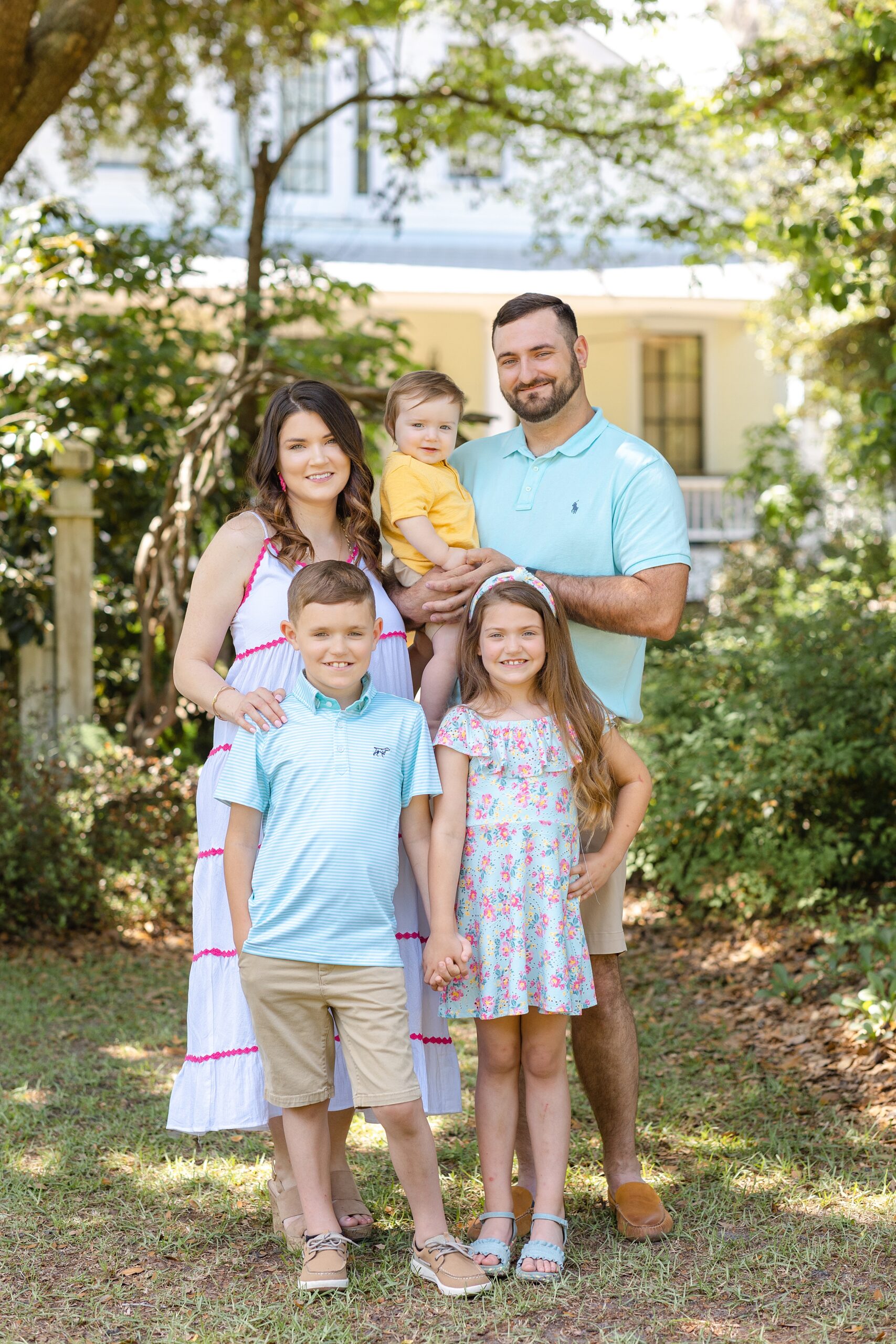 A family of five stand together in a home garden smiling and holding hands