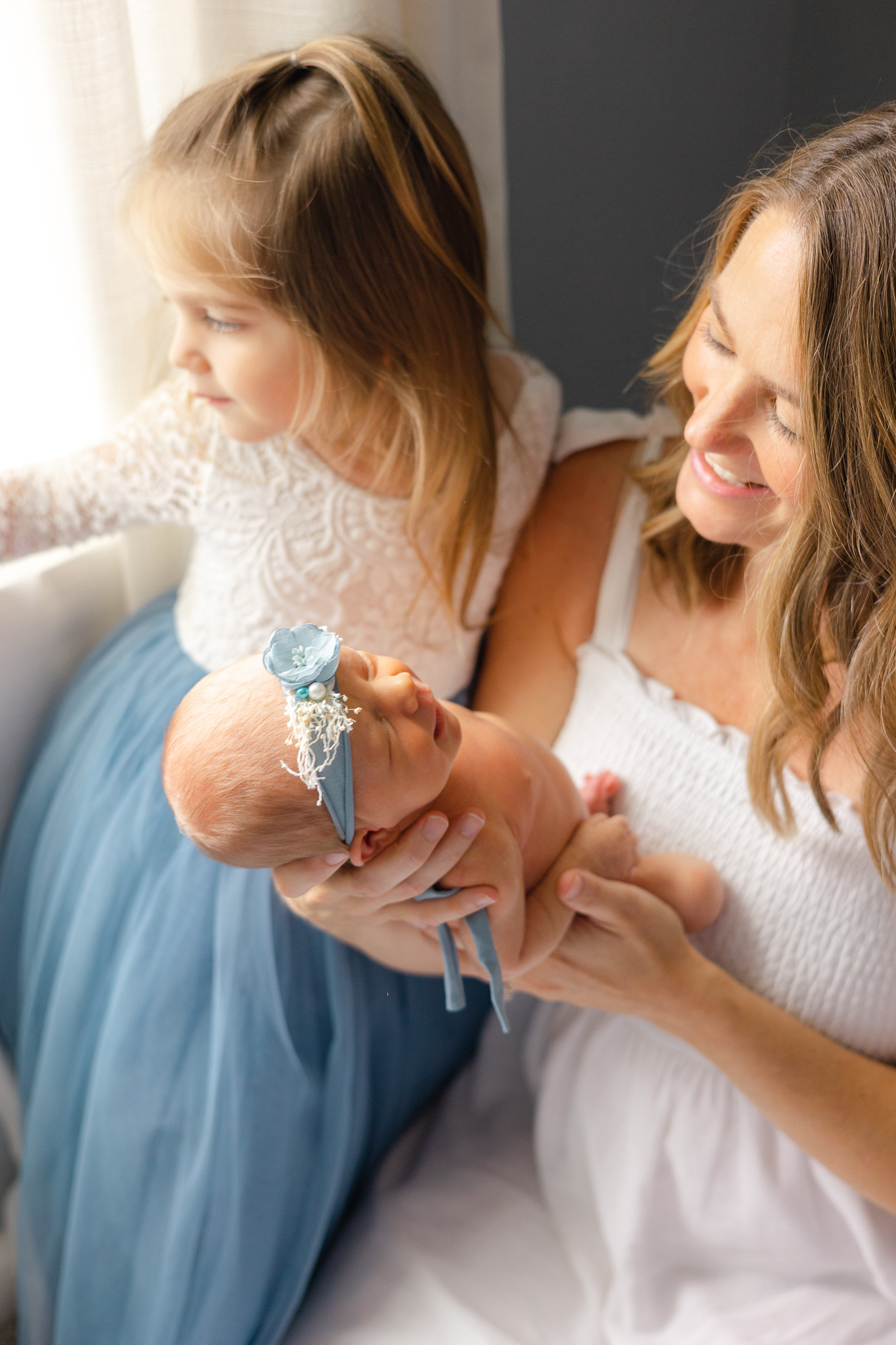 A mother sits in a chair by a window while holding her newborn baby in front of her southern sleep