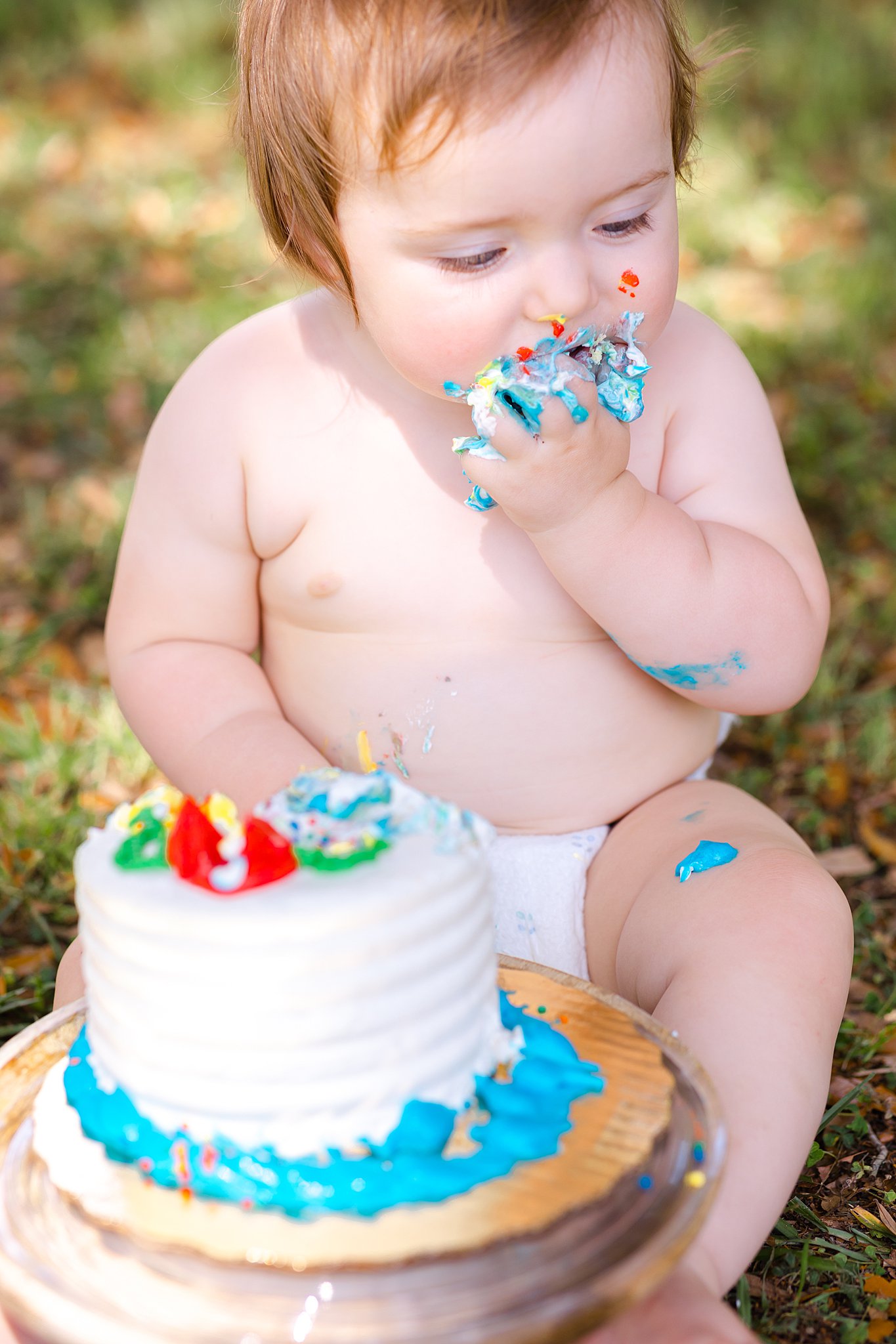 An infant sits in a park eating a birthday cake with its hands and making a mess after visiting daycares in savannah