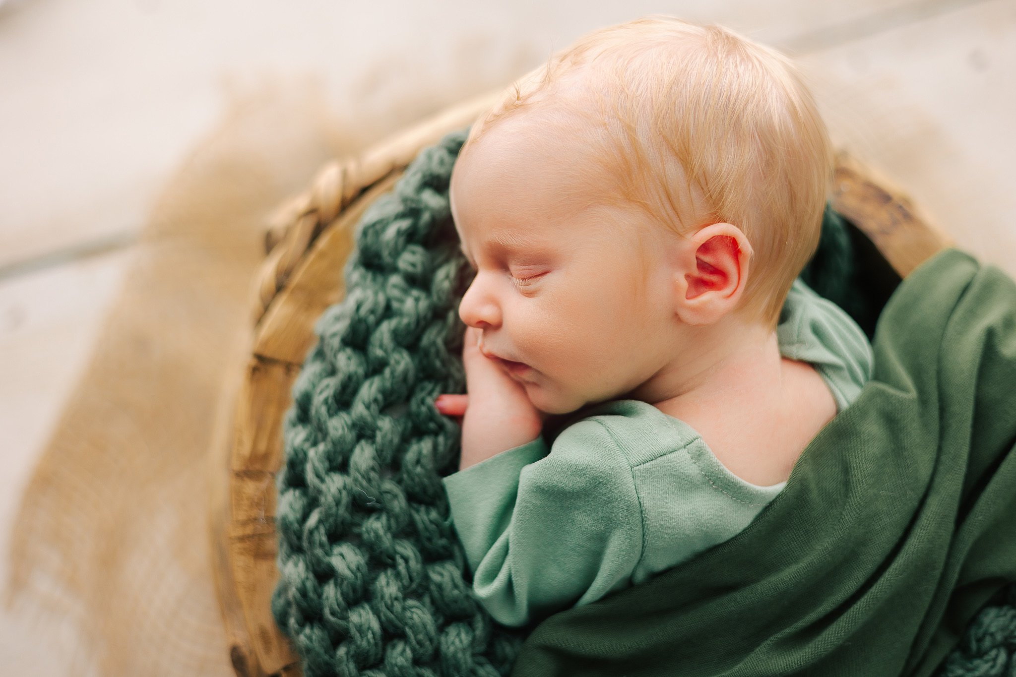 A newborn baby in a green onesie sleeps in a basket after visiting a savannah chiropractor
