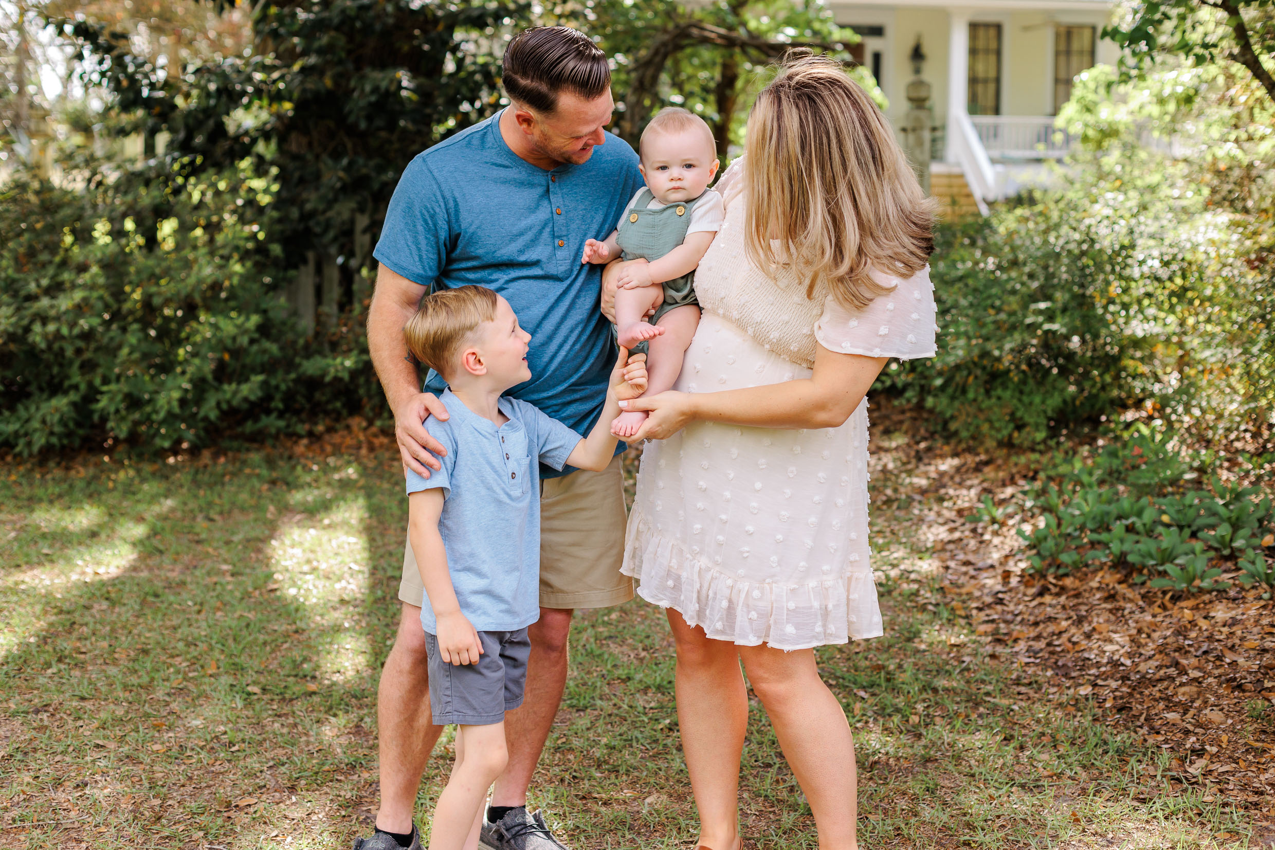 A mom, dad and young son all smile and tickle an infant in mom's arms