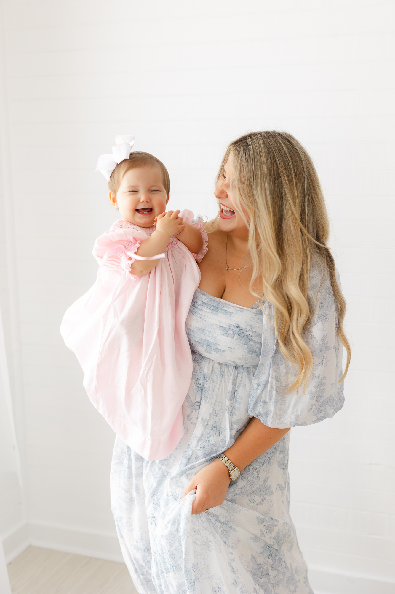 Young mom is wearing a blue dress from a client closet holding her little girl who is wearing a pink smocked dress