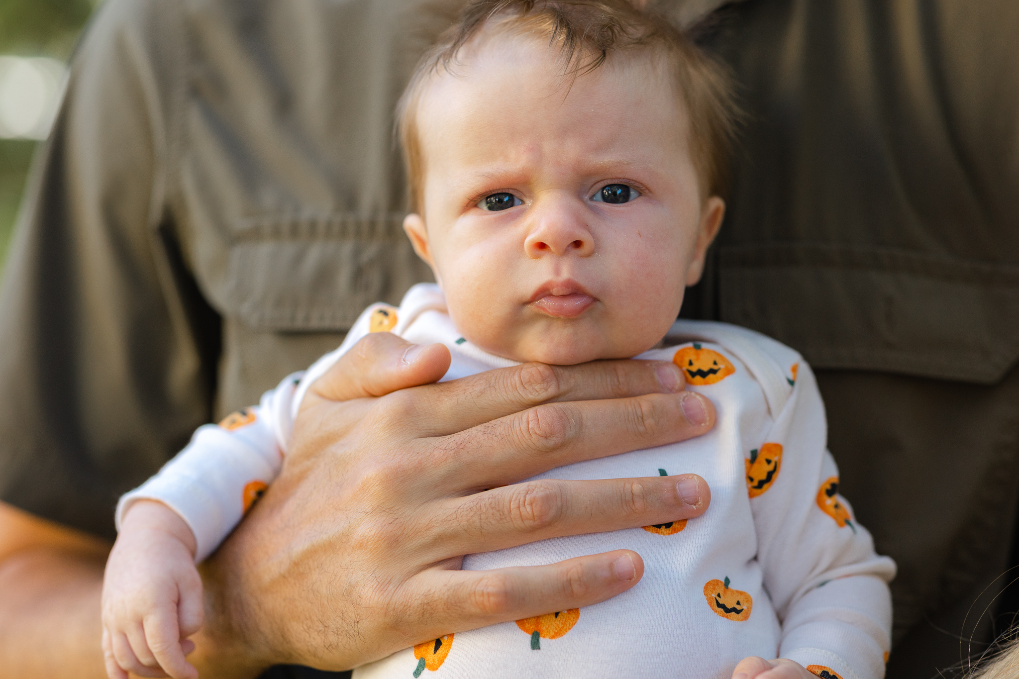 A newborn baby sits in dad's hands in a pumpkin onesie