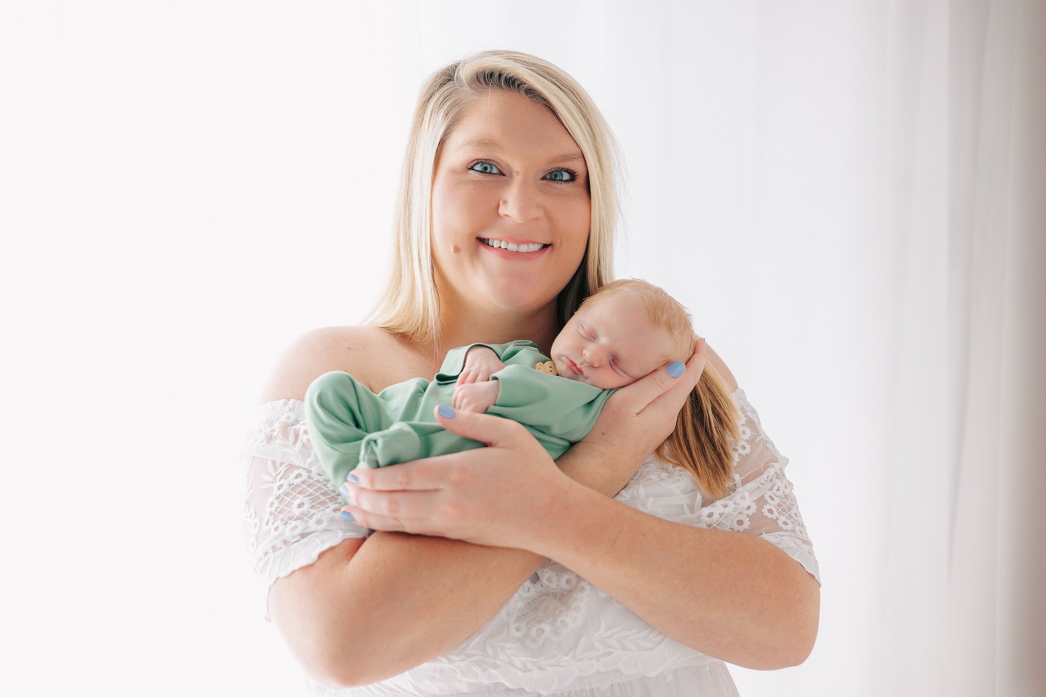 A happy new mom holds her sleeping newborn baby in her hands while standing in a studio window after getting help from a savannah obgyn