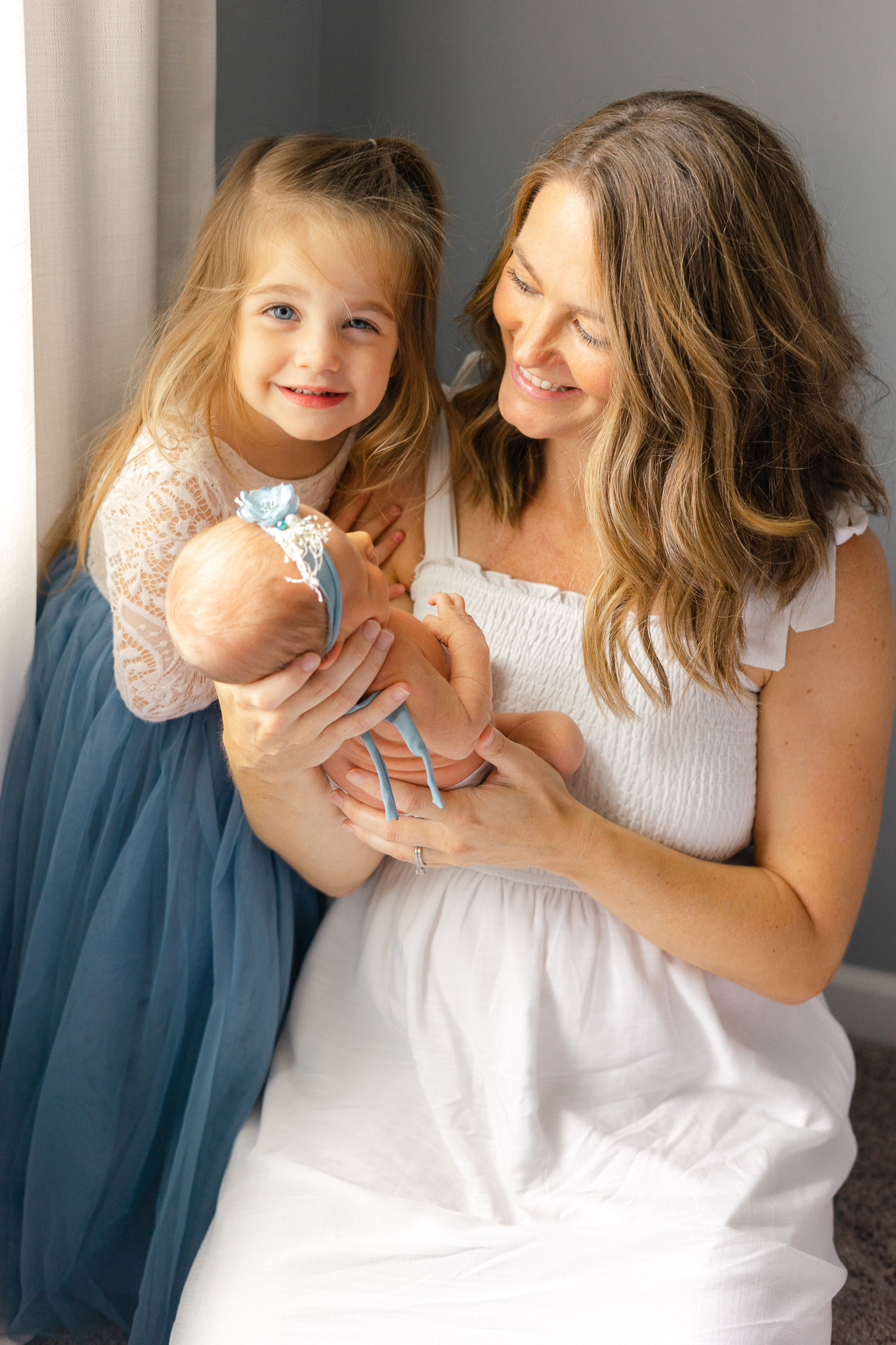 A mom and daughter sit in a window smiling down at a newborn baby in mom's hands during things to do in savannah with toddlers