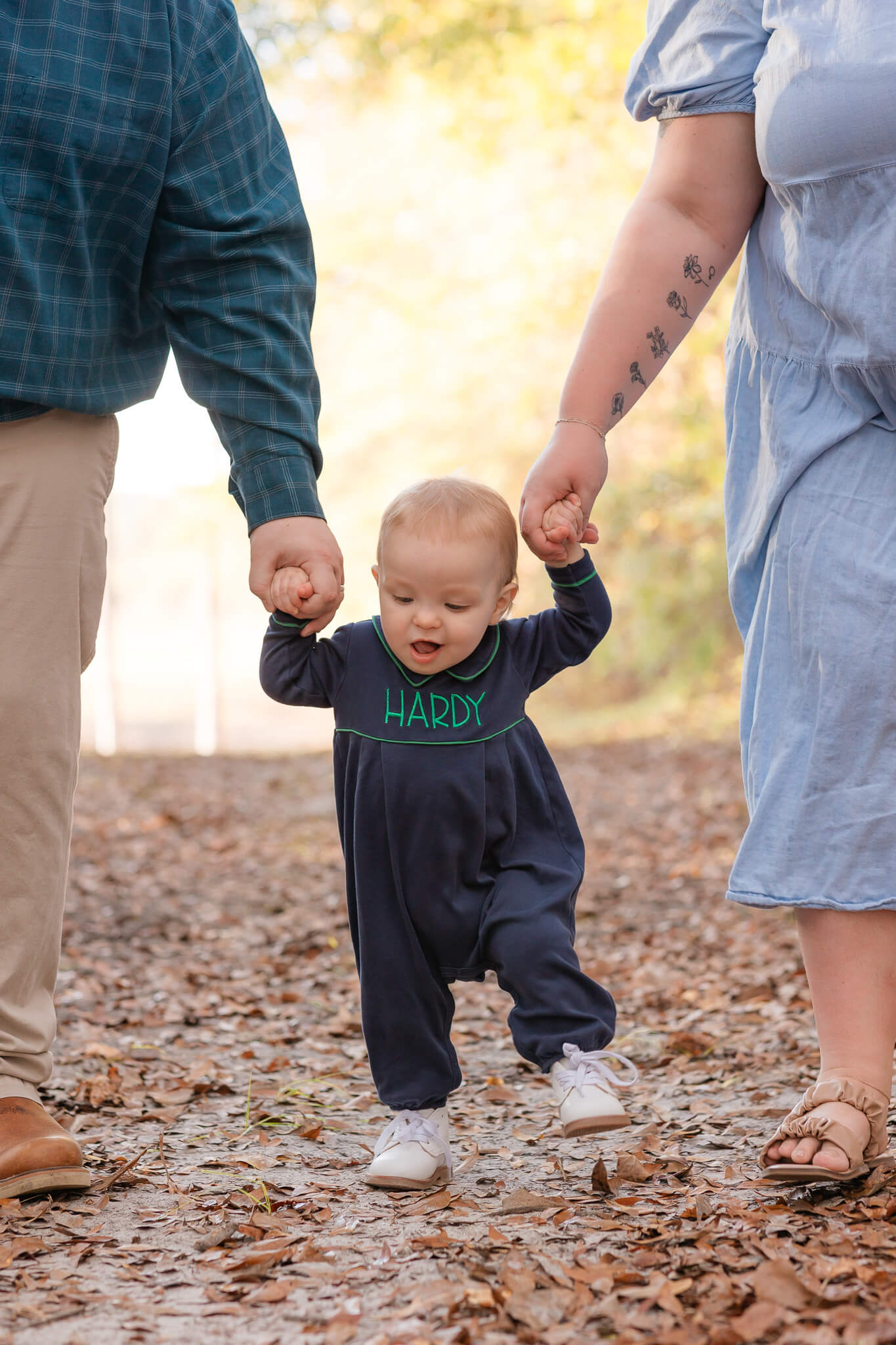 one year old holding mom's and dad's hand and trying to walk. Outdoor session in Savannah, Ga with Constance Calton photography