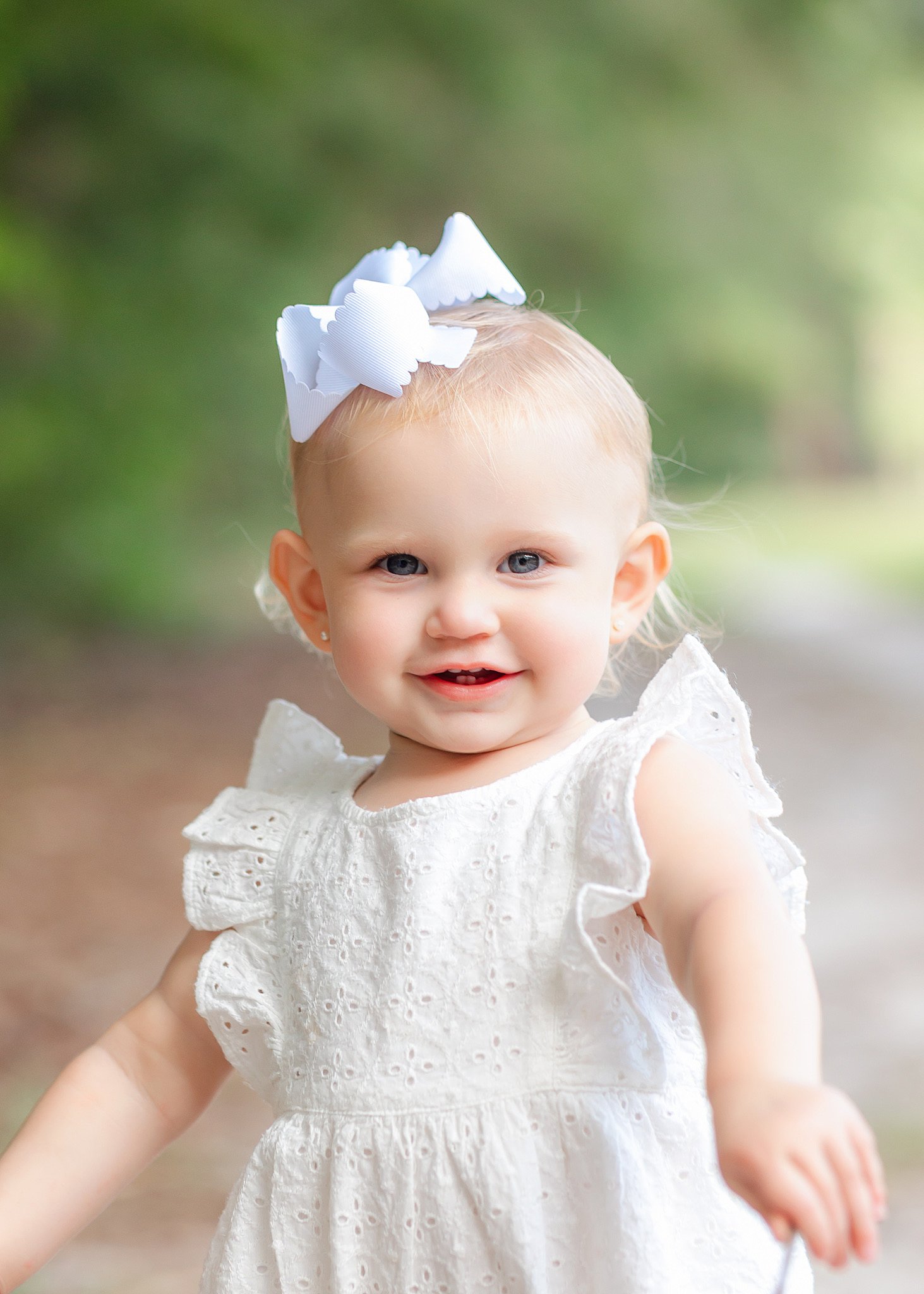 A baby girl in a white dress plays in a park with a big smile