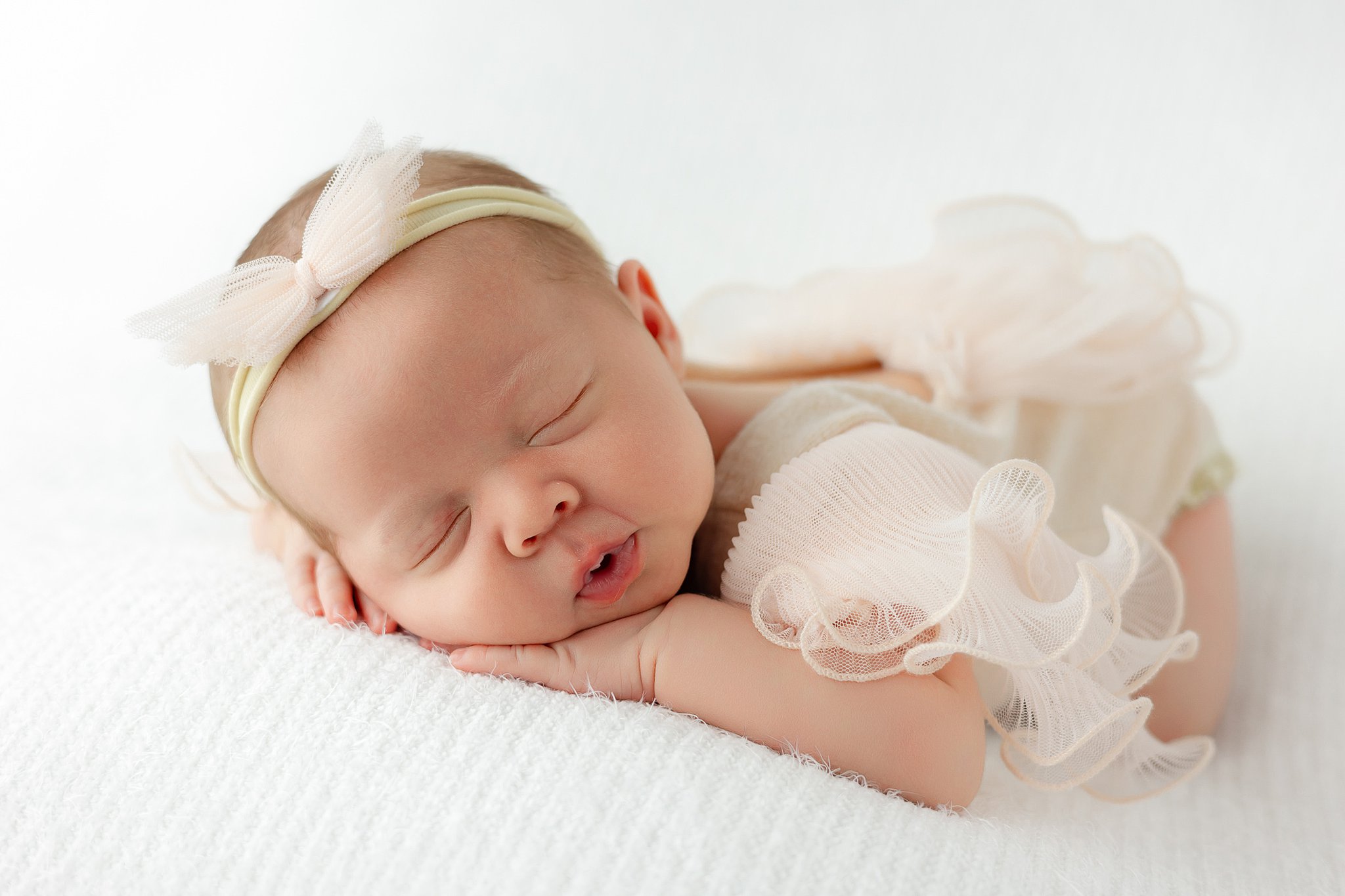 A newborn baby girl sleeps on a white bed in a frilly dress and headband after meeting Lactation Consultants in Savannah, GA