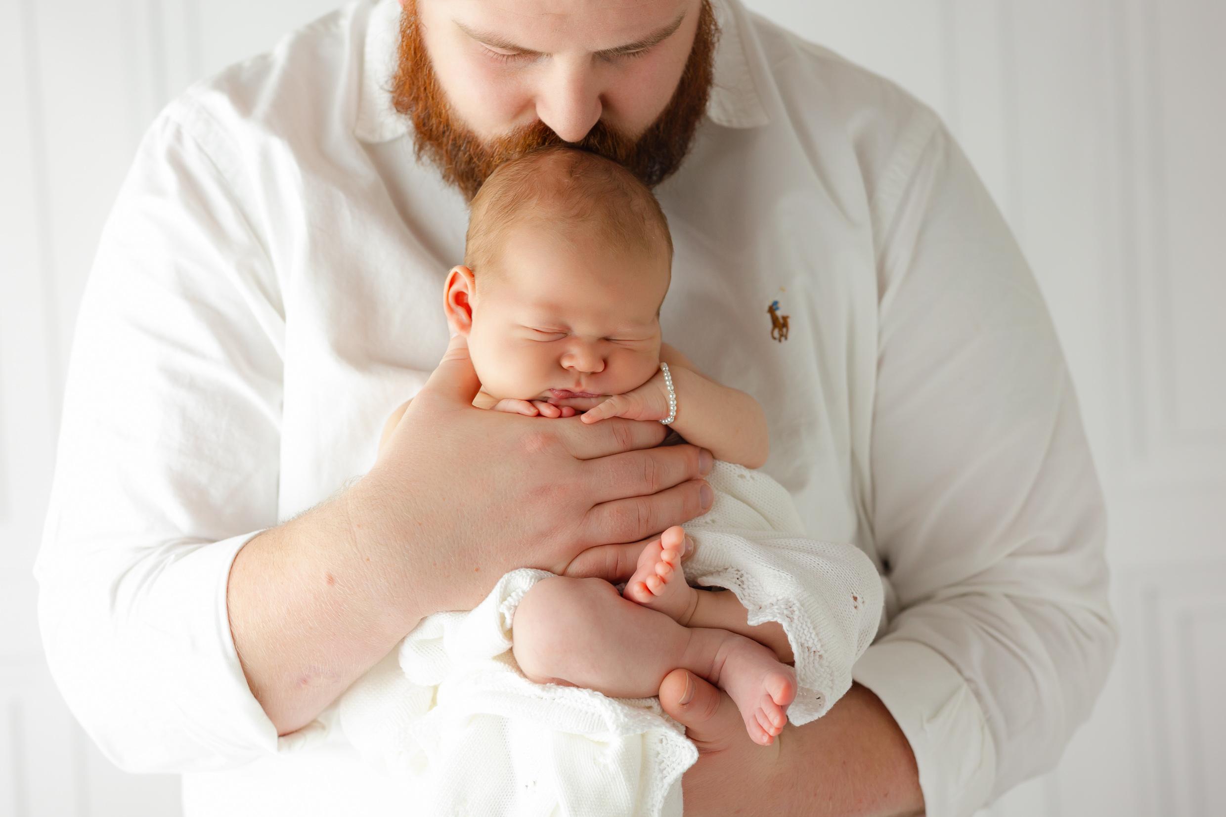 A new dad kisses the head of his sleeping newborn daughter in his hands