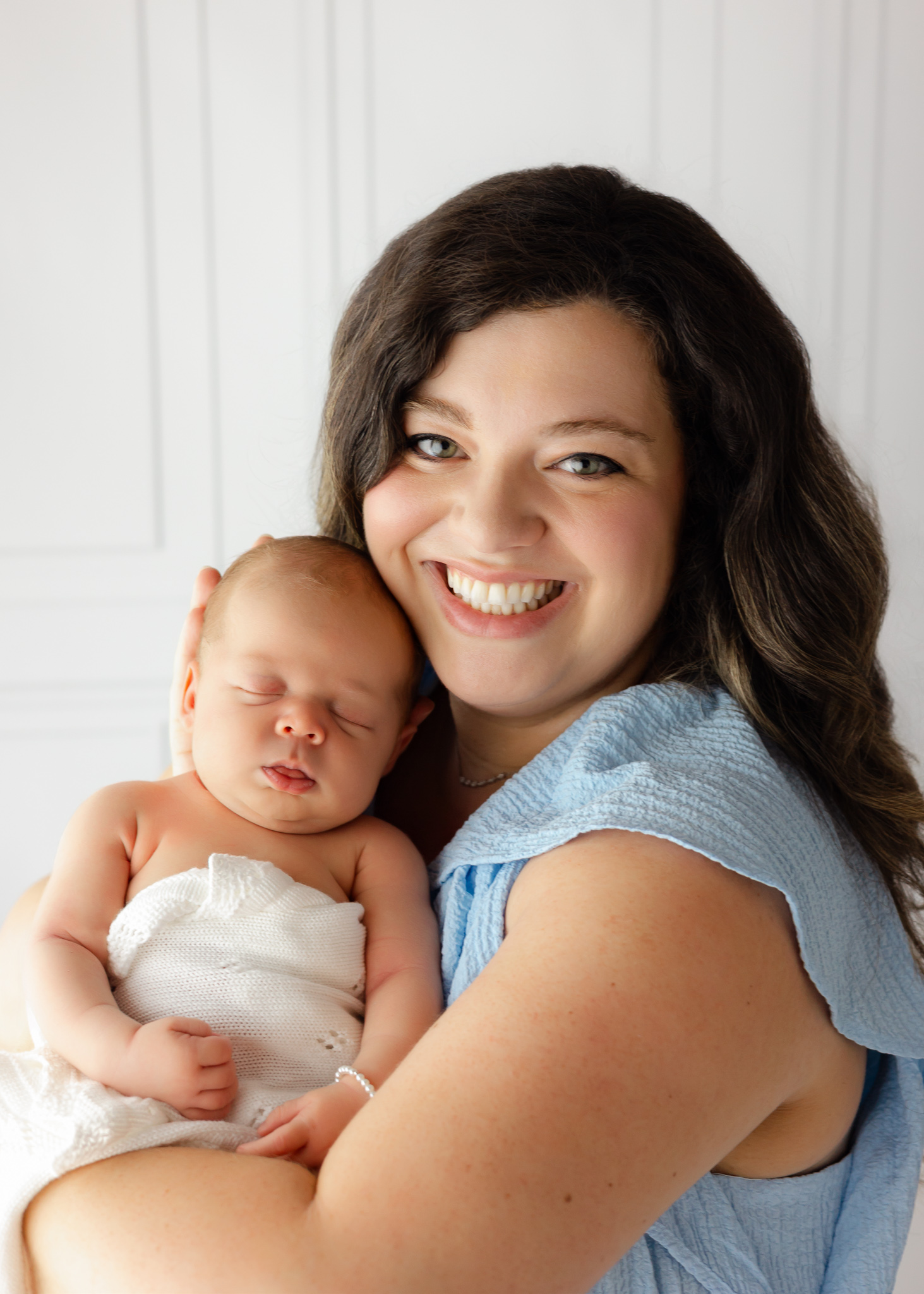 A happy mom smiles with her sleeping newborn baby in her arms in a studio after meeting Georgia's Dream Nannies