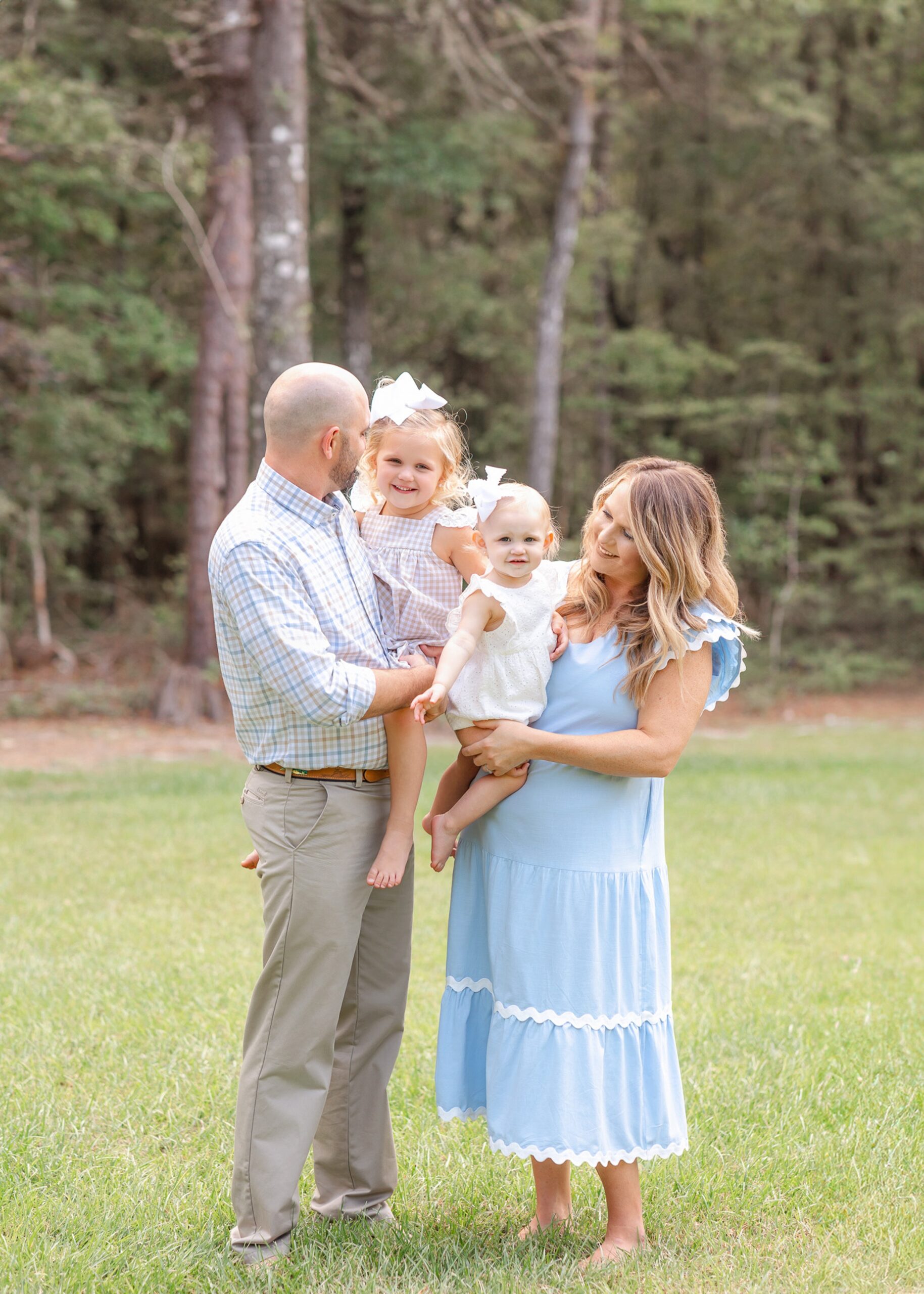 A happy family of 4 stand in a lush lawn smiling before visiting Exhilarate Savannah