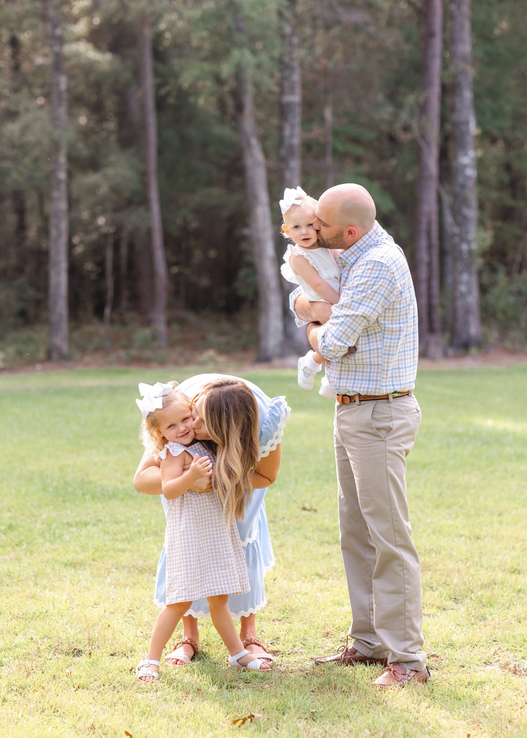 Happy mom and dad kiss their baby girls while playing in a lawn before visiting Exhilarate Savannah