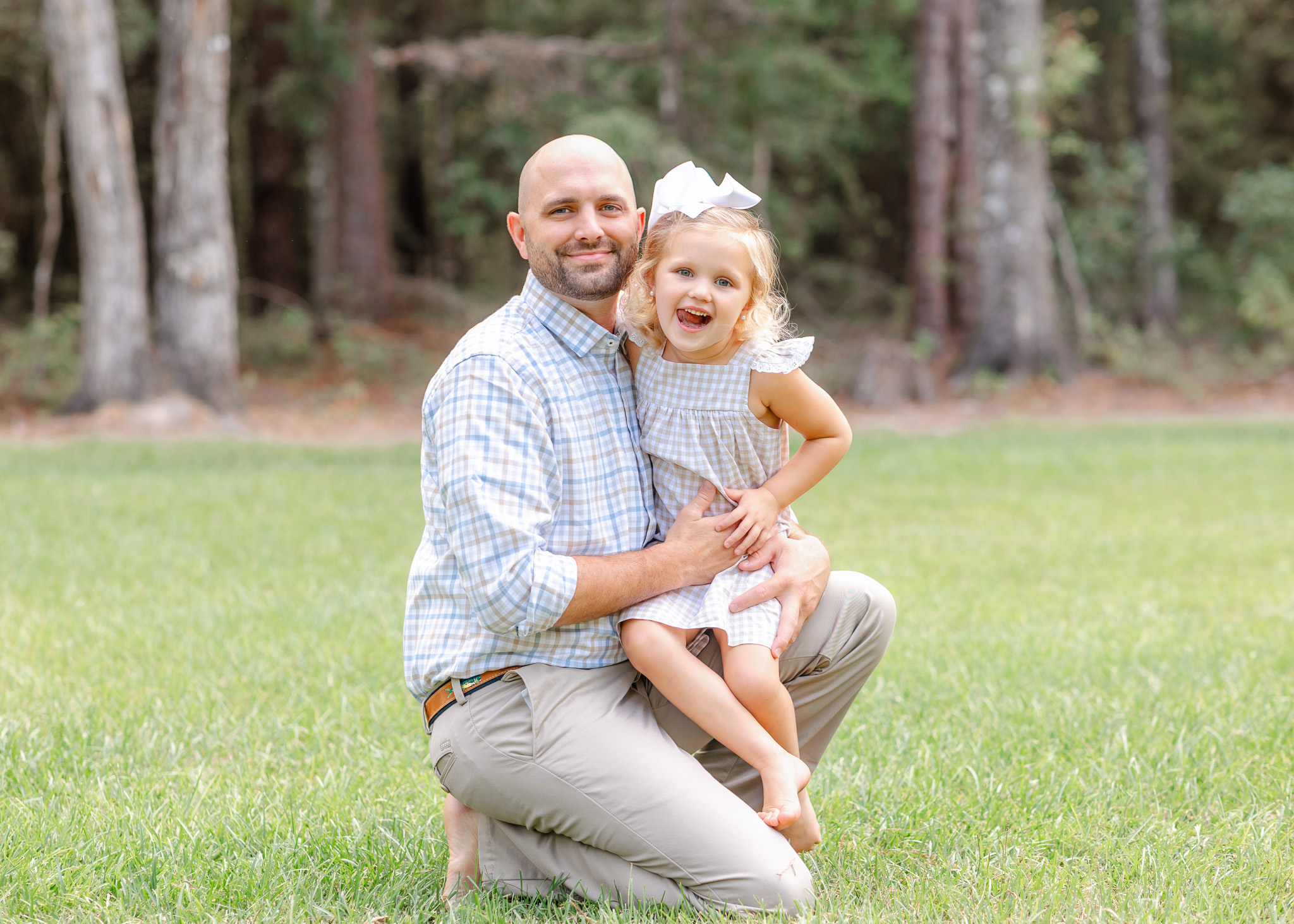 A proud dad kneels in a park lawn with his silly toddler daughter sitting on one knee after some parenting classes in Savannah, GA