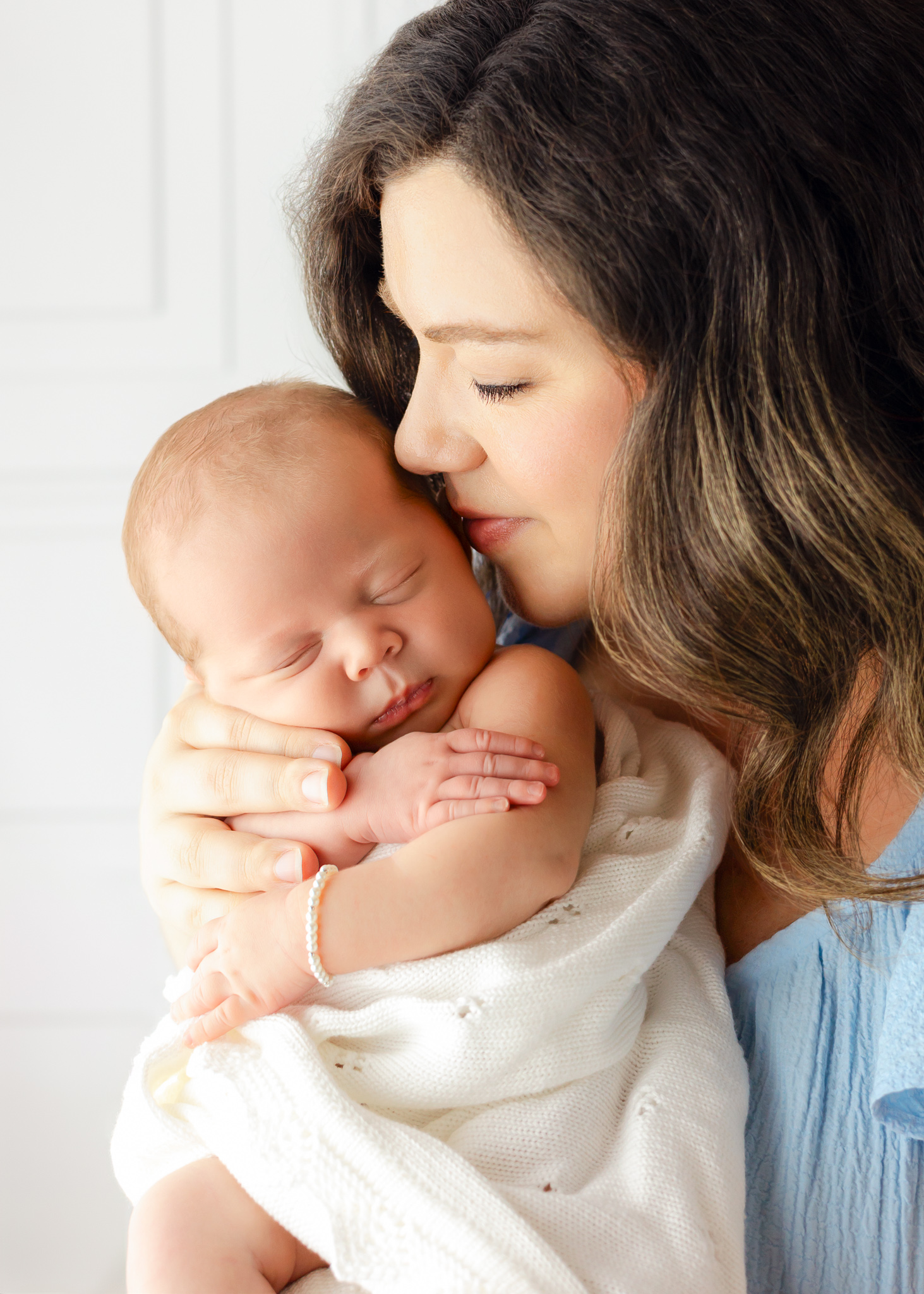 A newborn baby sleeps on mom's chest as she is kissed while standing in a studio