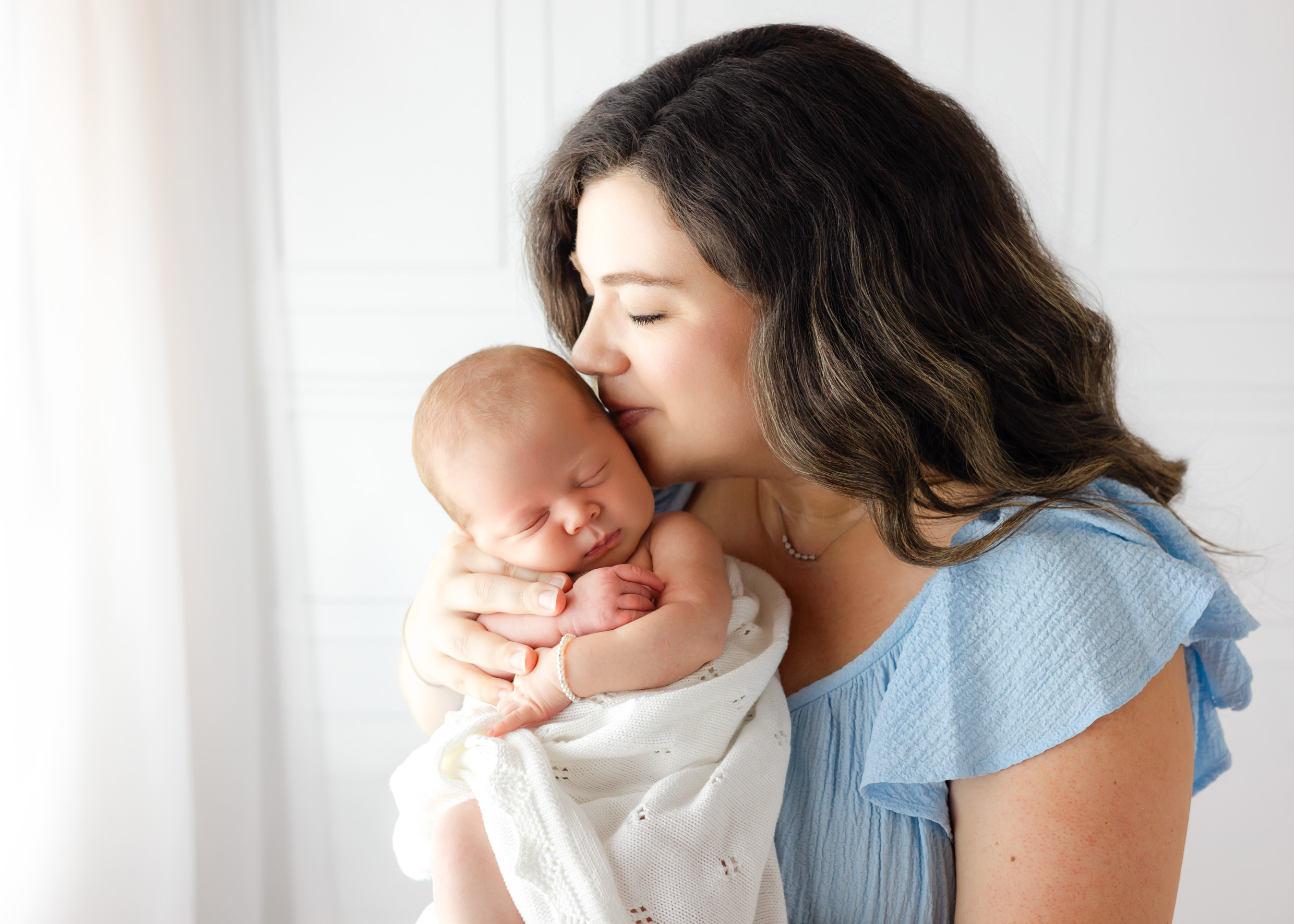 A happy new mom in a blue dress kisses the head of her sleeping newborn daughter in hr hands after finding placenta encapsulation in Savannah, GA