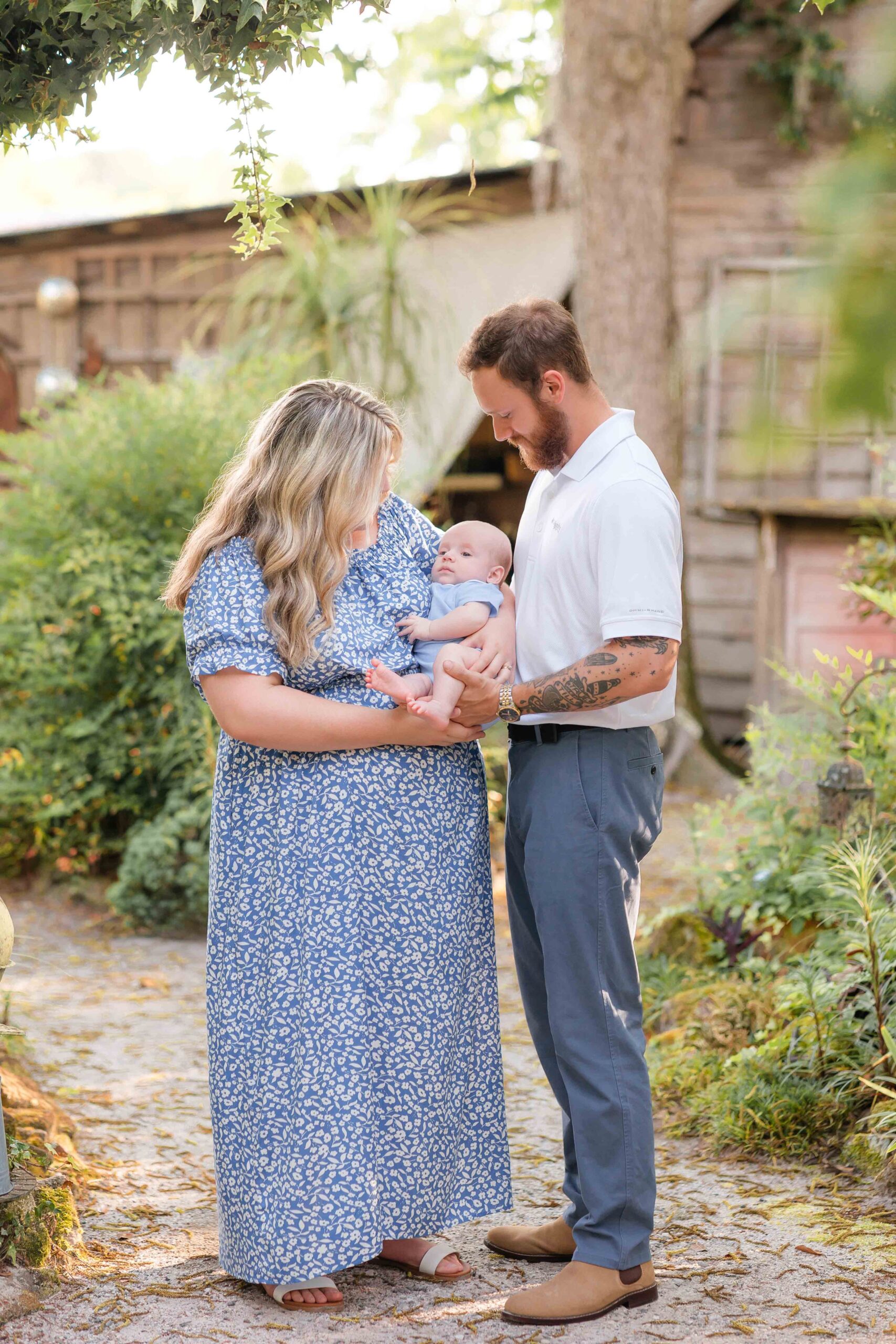 Happy new parents snuggle their newborn baby in their arms while exploring a garden