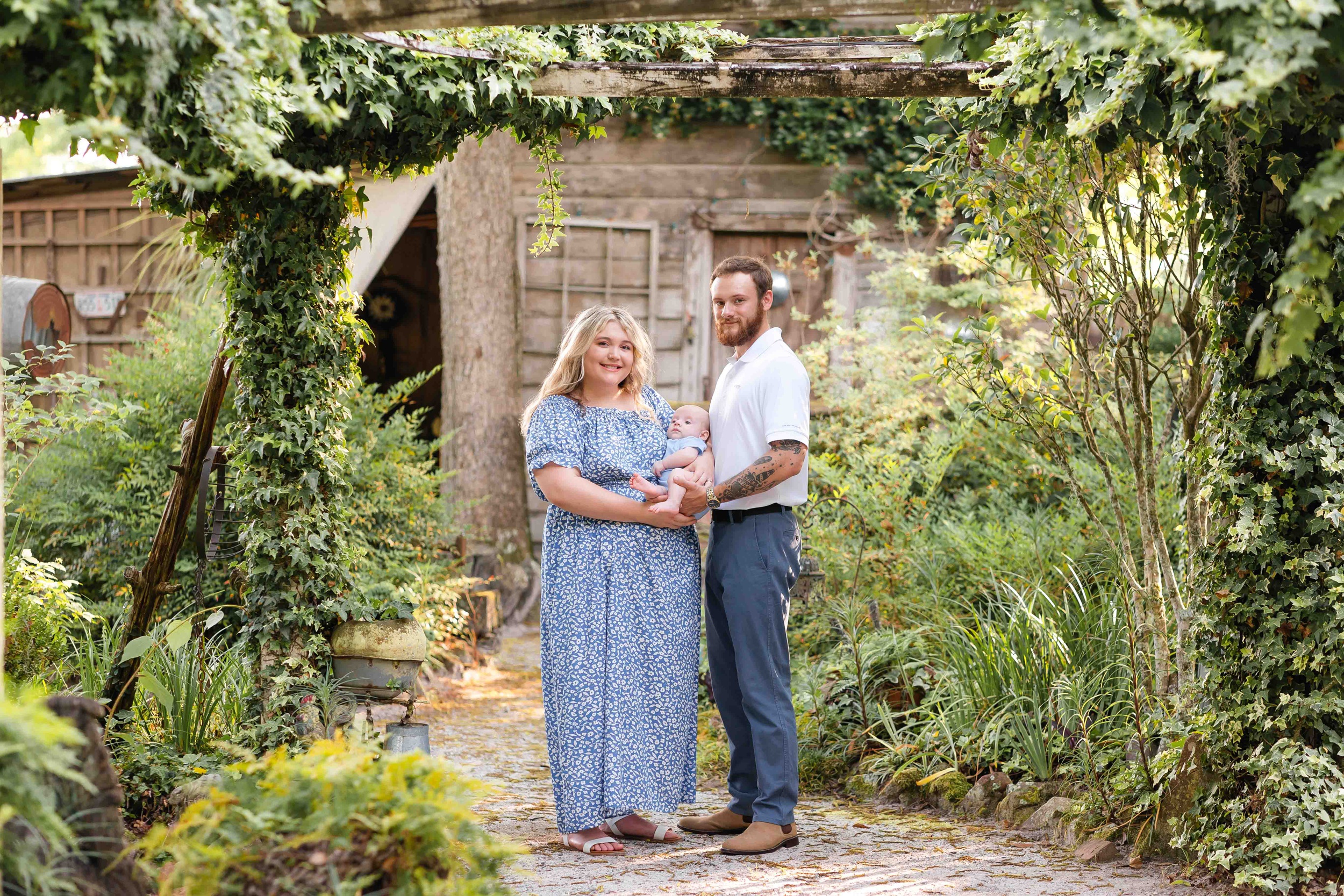 Happy new parents stand in a thriving garden holding their newborn baby after visiting a toy store in savannah