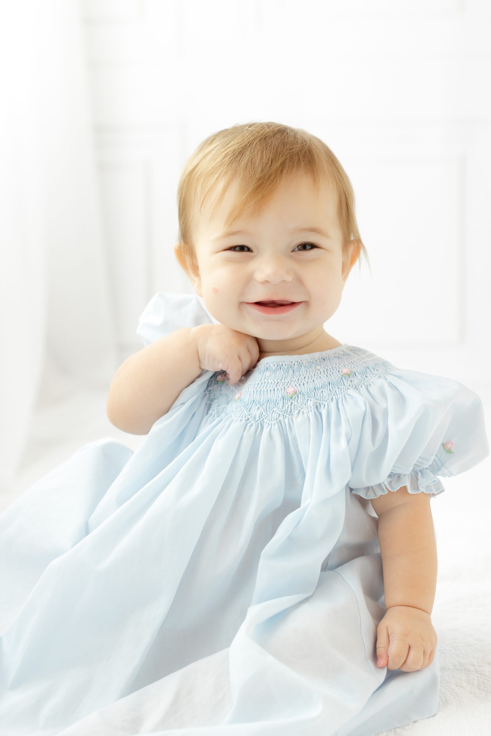 A smiling baby in a blue dress sits in a studio before her birthday party in Pooler, GA