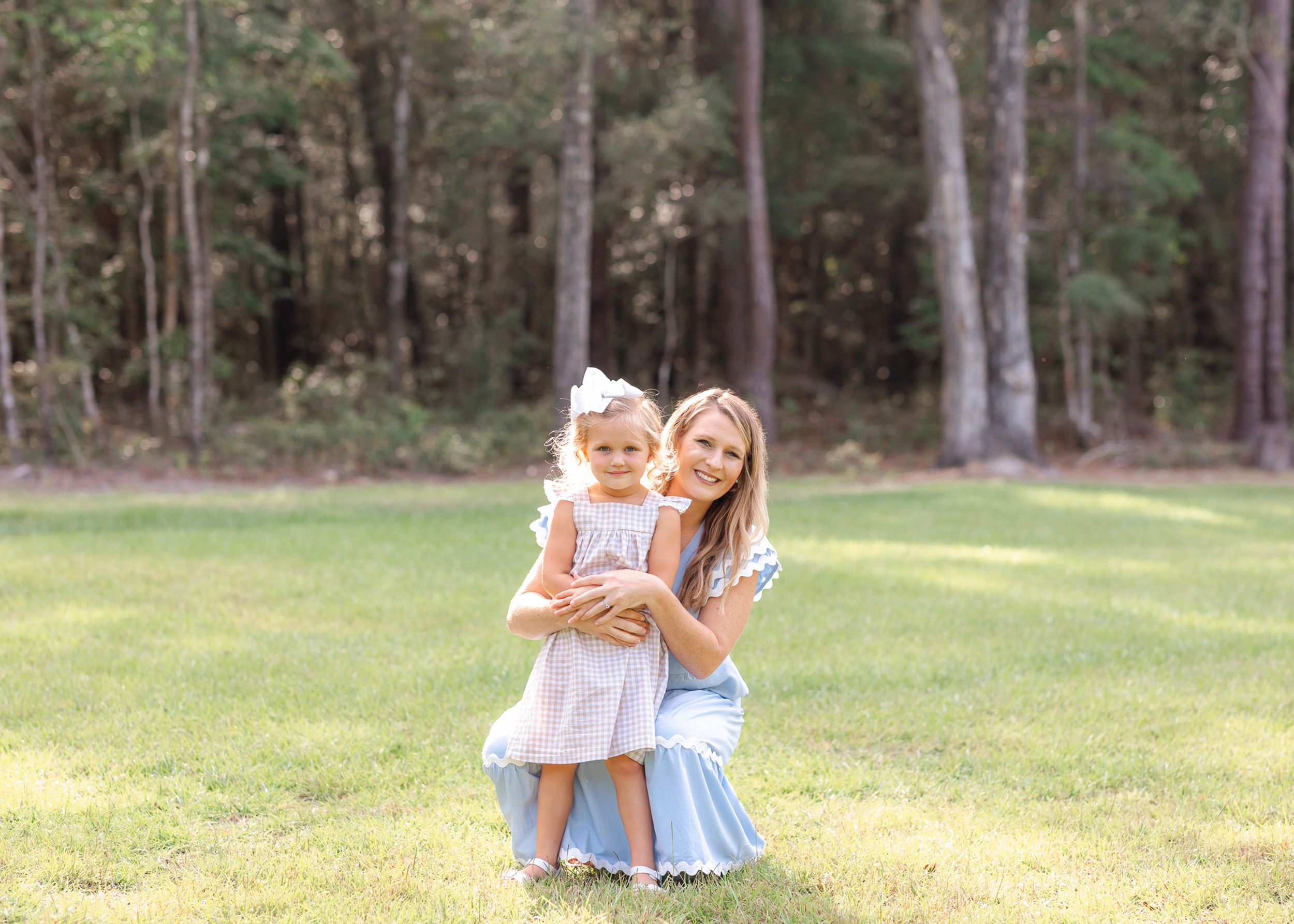 A mom in a blue dress kneels down to hug her toddler daughter in a dress after visiting a Child Therapist in Savannah, GA