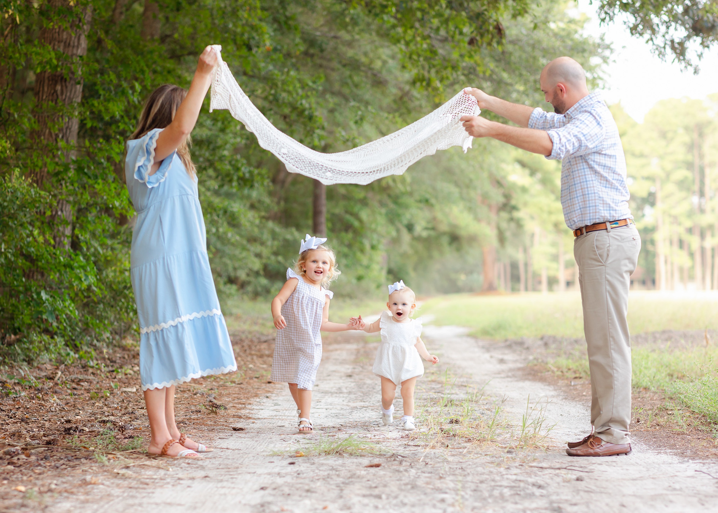 A mom and dad lifts a blanket over their two running toddler daughters