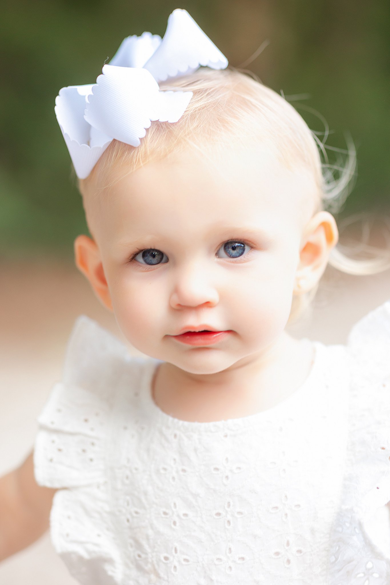 A toddler in white dress and bow stands in a park after visiting Family friendly places to stay in Savannah, GA