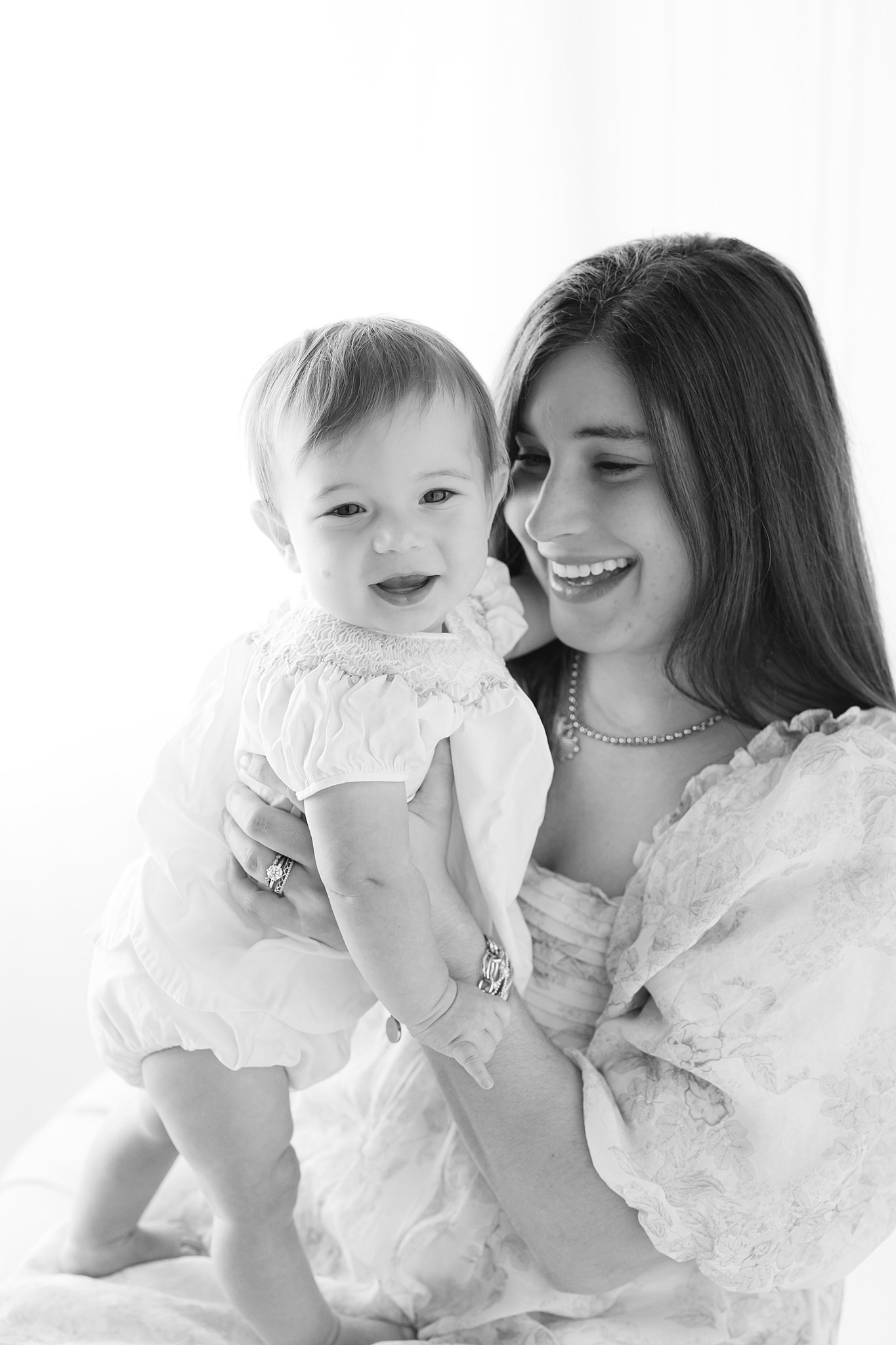 A mom and her baby daughter laugh while playing in a studio in dresses