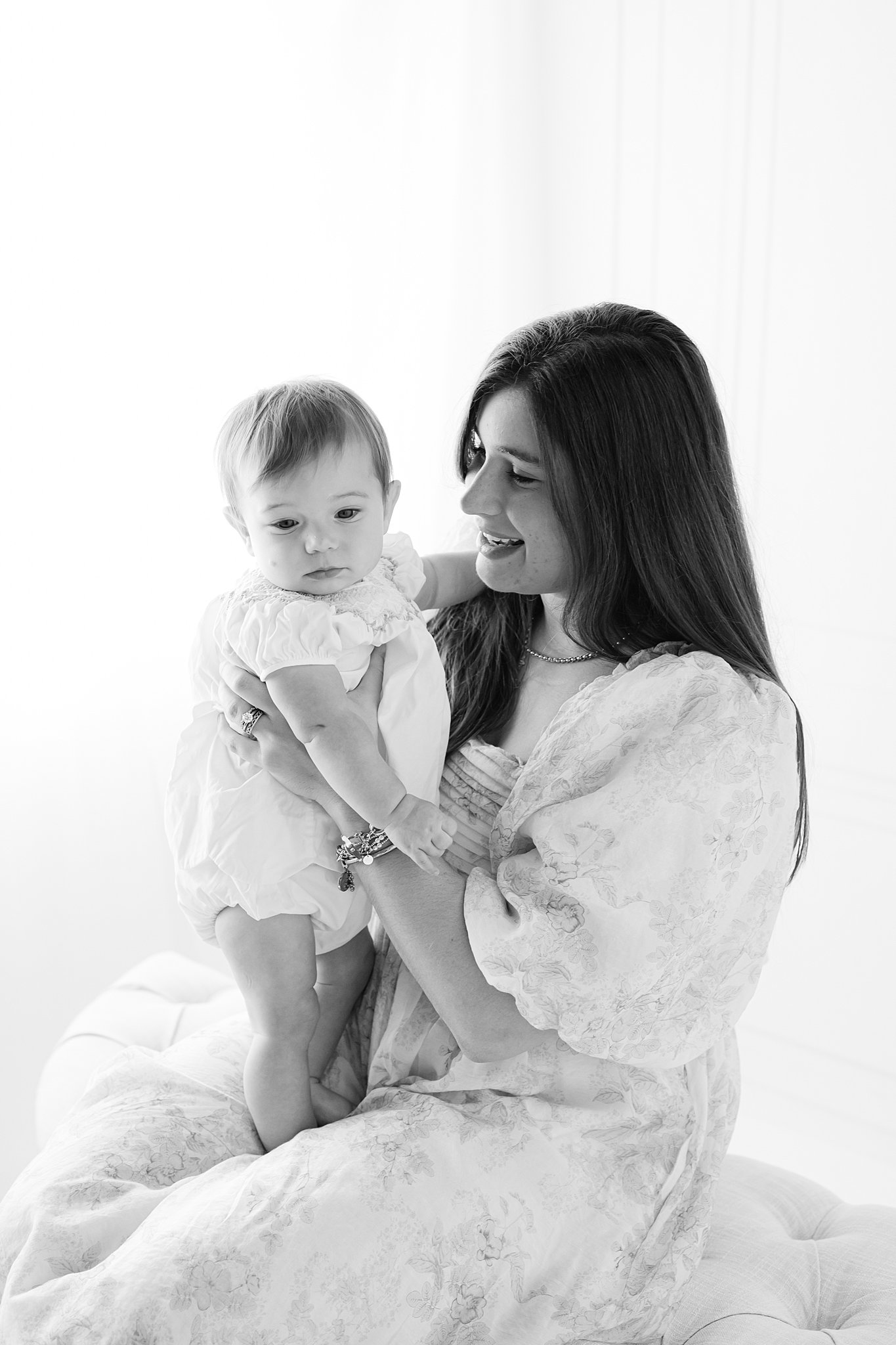 A baby girl stands in mom's lap on a bench in a studio thanks to an obgyn in Rincon, GA