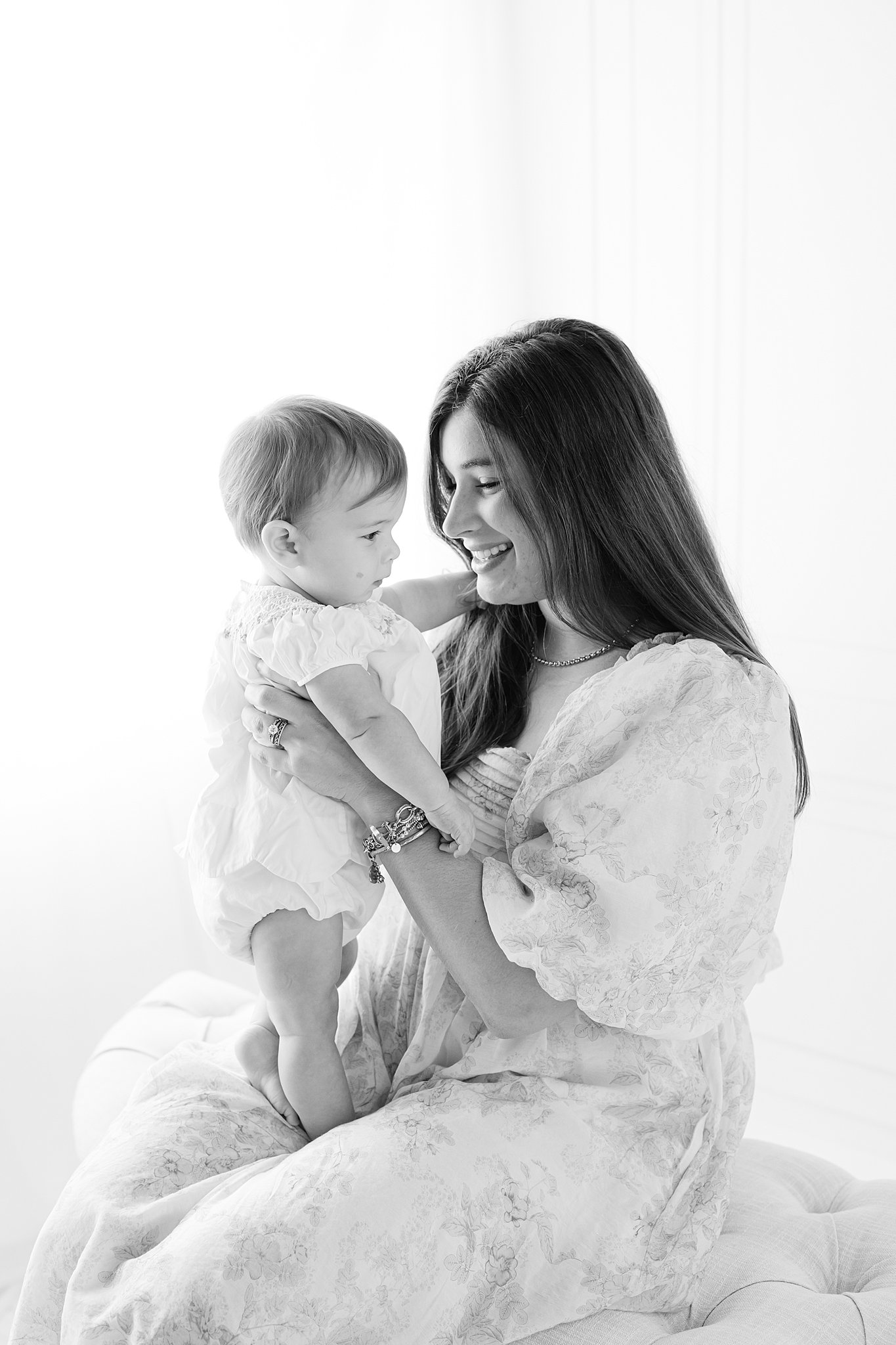 A happy mom plays with her baby in her lap on a bench in a studio in black and white thanks to an obgyn in Rincon, GA