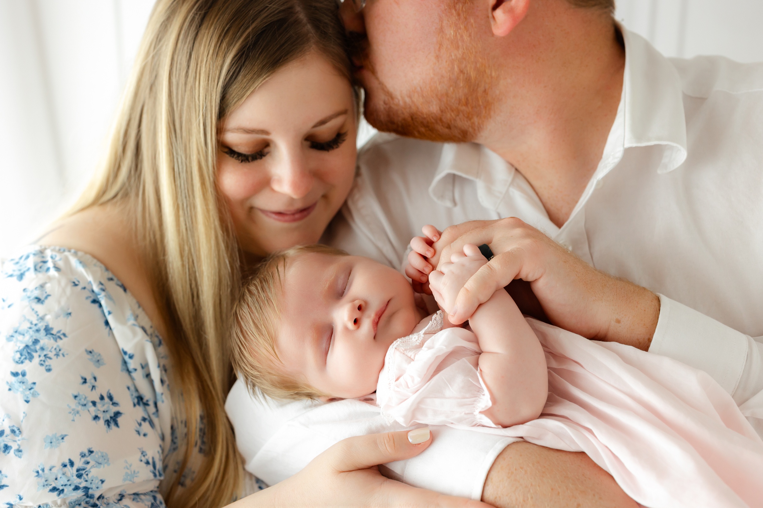 A happy newborn sleeps in mom and dad's arms after visiting pediatric dentists in Pooler, GA