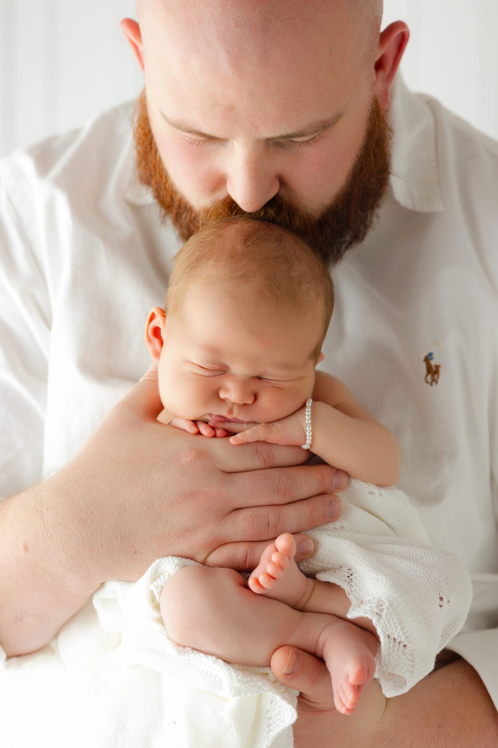 A new dad kisses the head of his sleeping newborn baby in his hands after visiting Pink Chicken Savannah