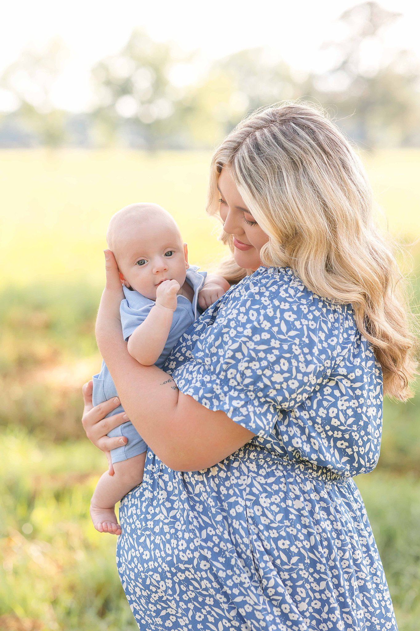 A happy mom in a blue floral dress smiles down at her baby in blue pajamas