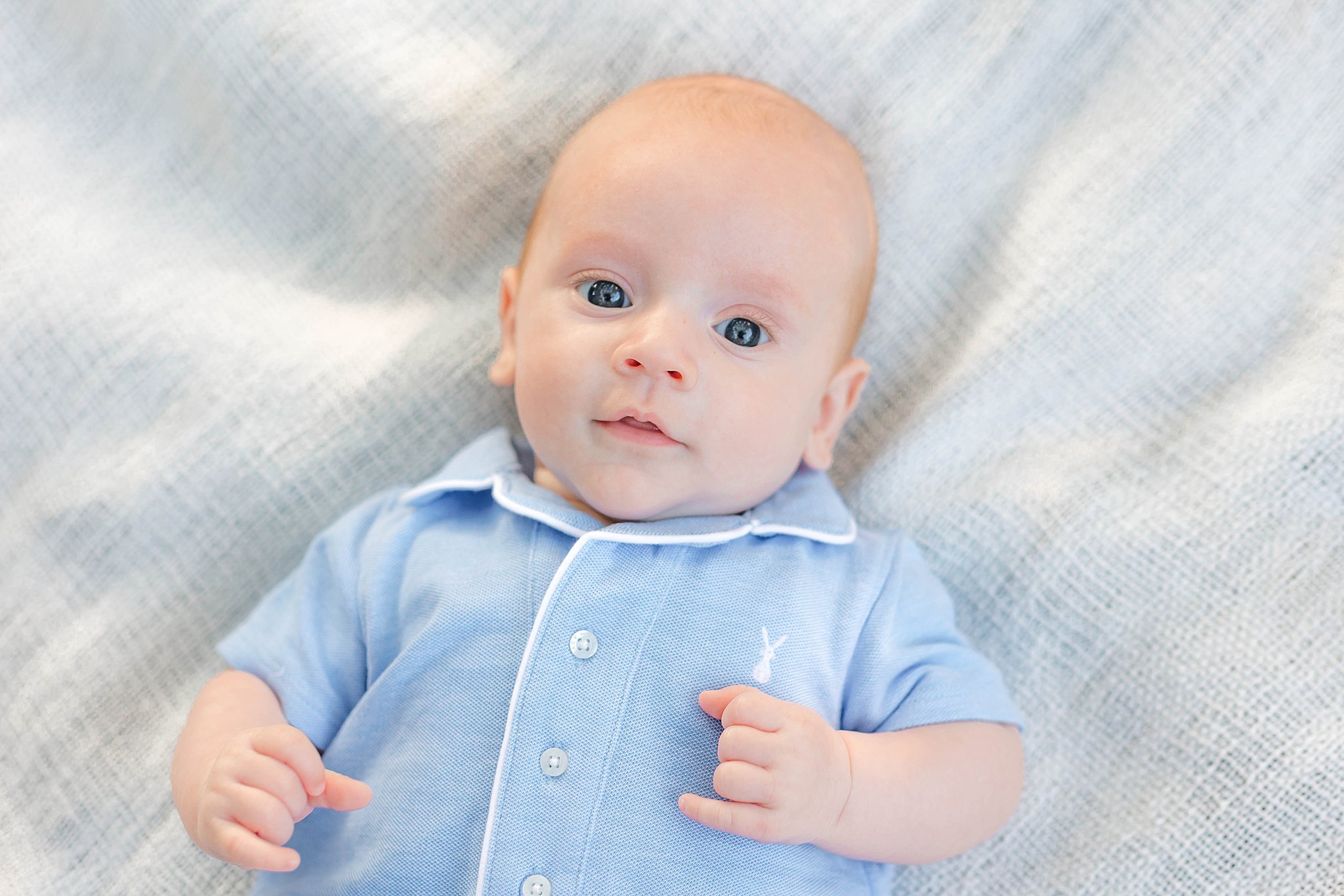 A baby lays on a bed in blue pajamas with eyes open before visiting pools in Savannah, GA