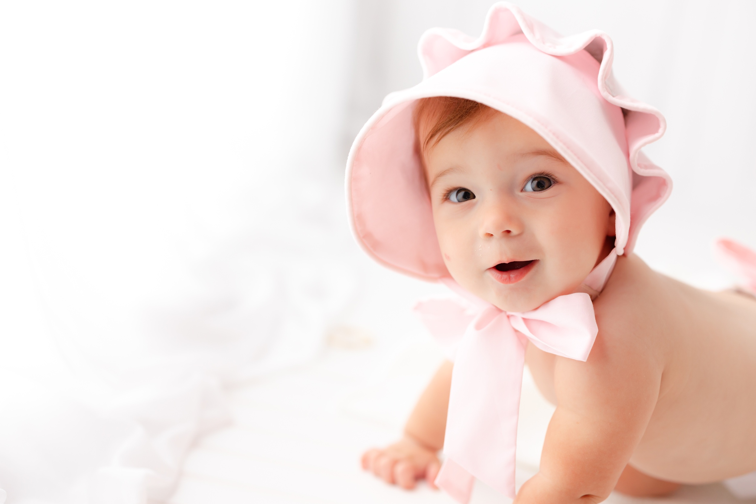 A baby crawls on a bed in a pink bonnet